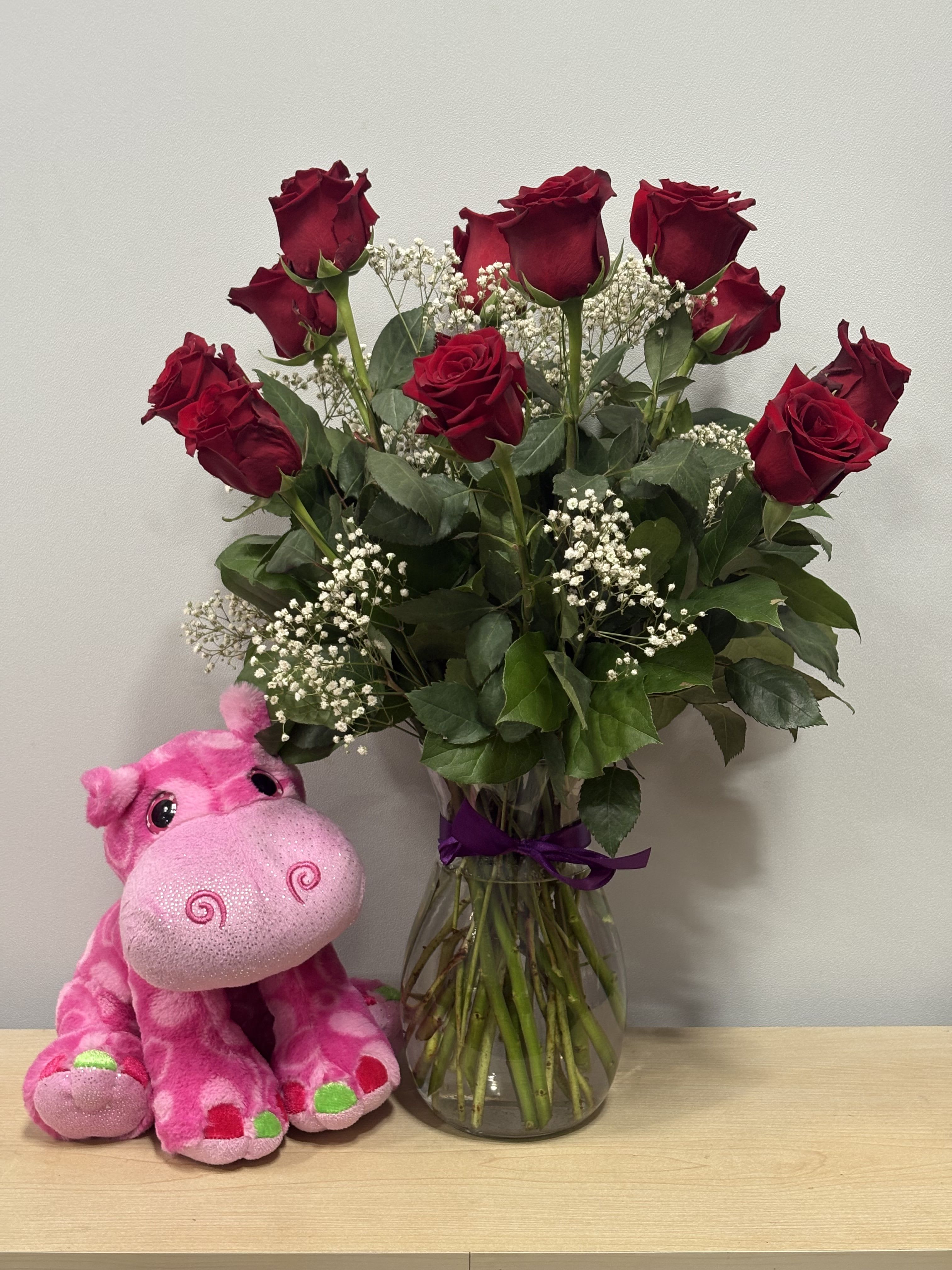 Red roses in a glass vase beside a pink plush hippo