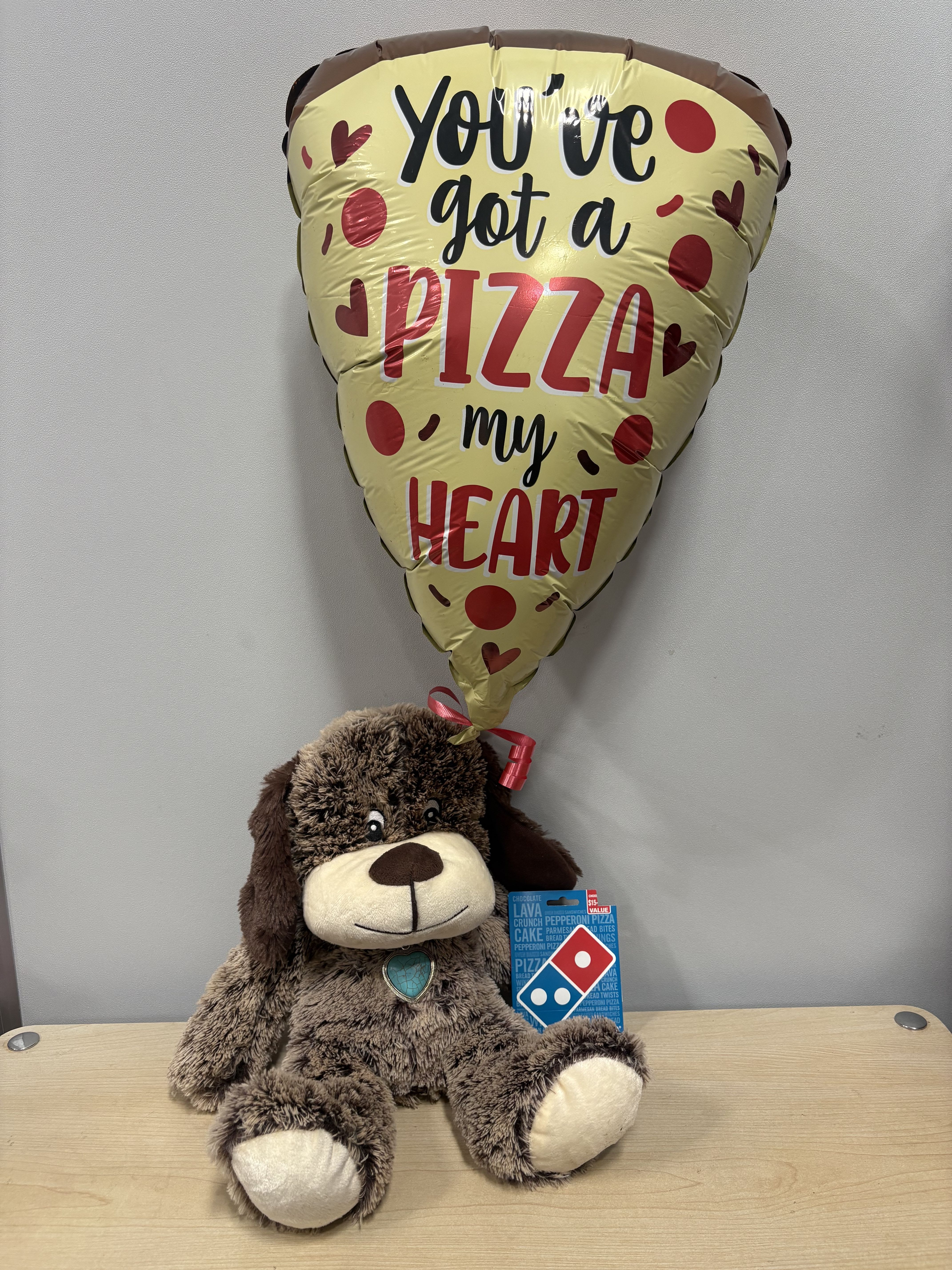 Pizza-shaped balloon above a plush dog holding a Domino's gift card