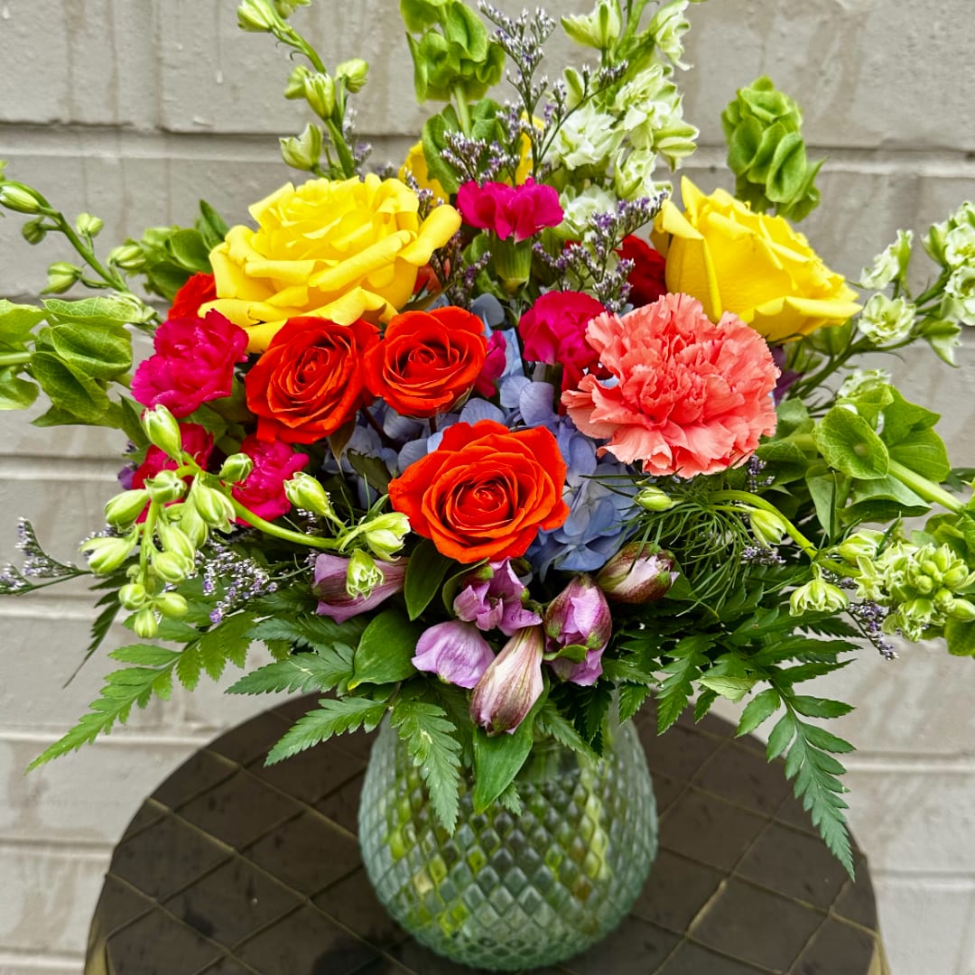 Colorful bouquet of roses, carnations, and other blooms in a textured glass vase