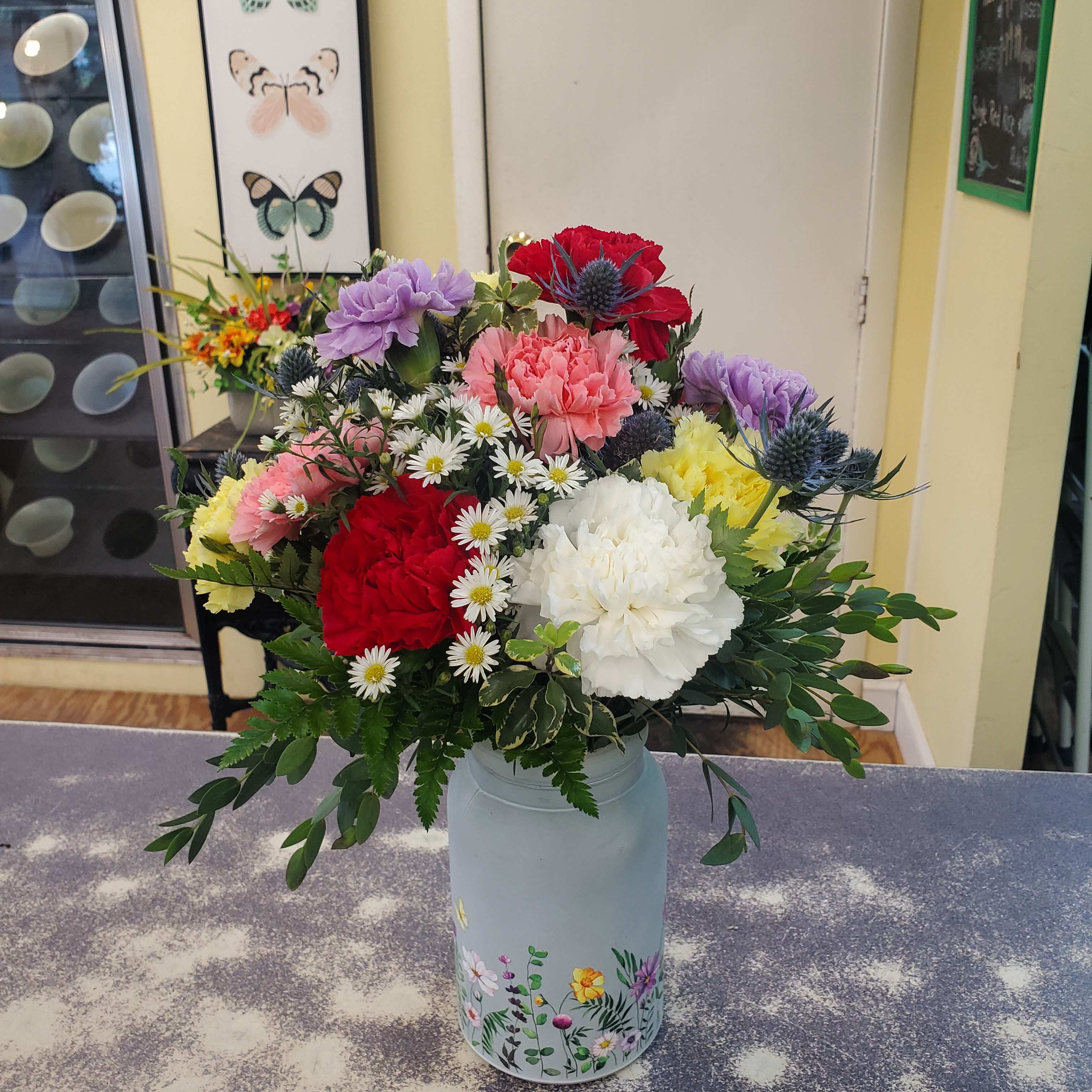 Mixed bouquet of carnations and daisies in a painted metal vase