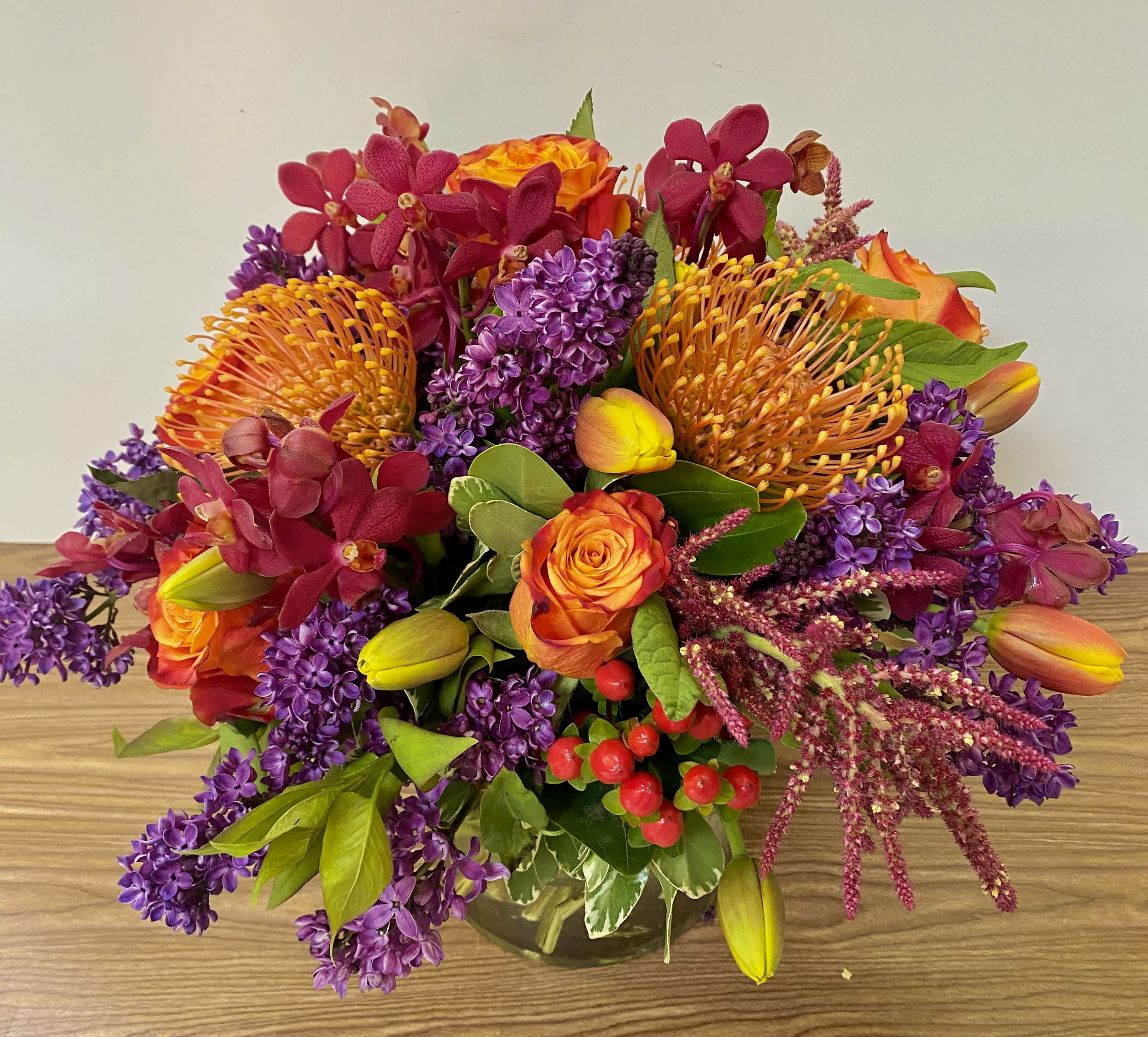 Bright mixed bouquet with orange roses, purple blooms, and yellow tulips in a glass vase