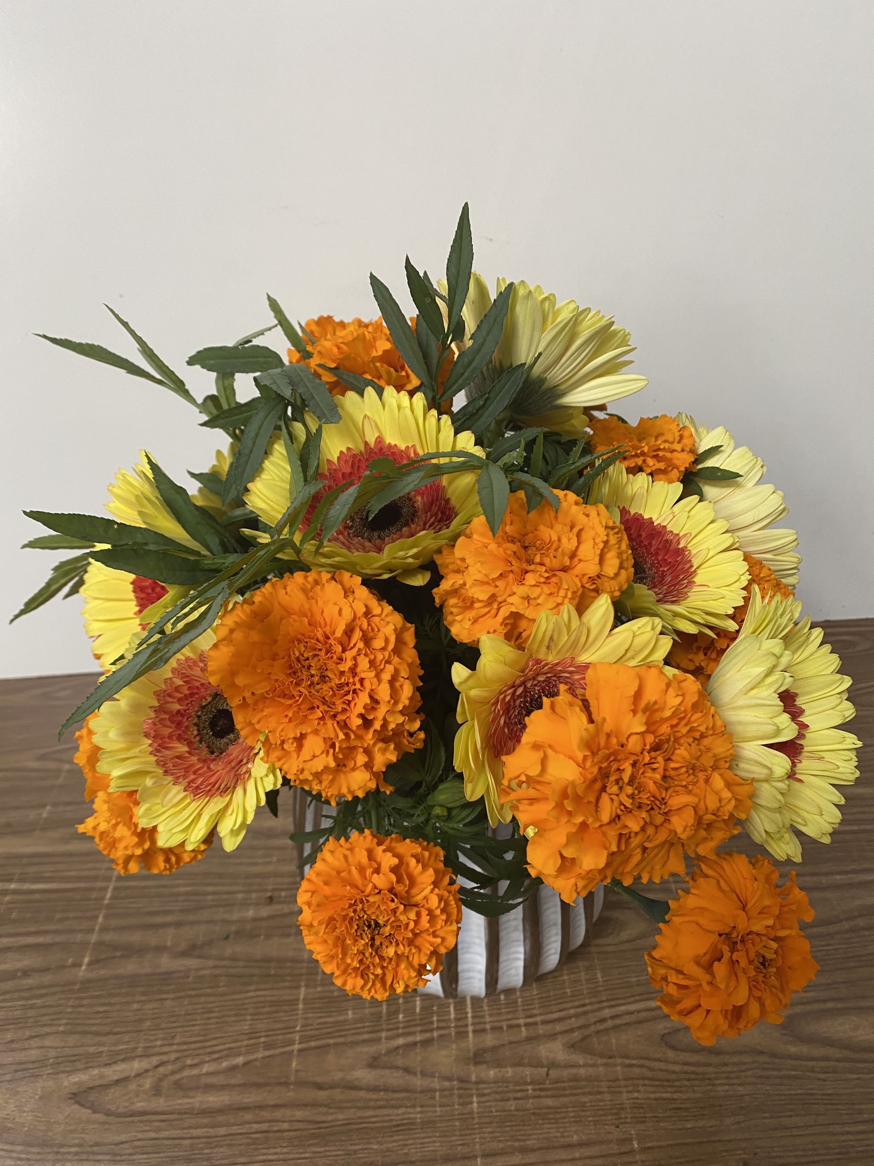 Bouquet of yellow gerbera daisies and orange marigolds in a white vase