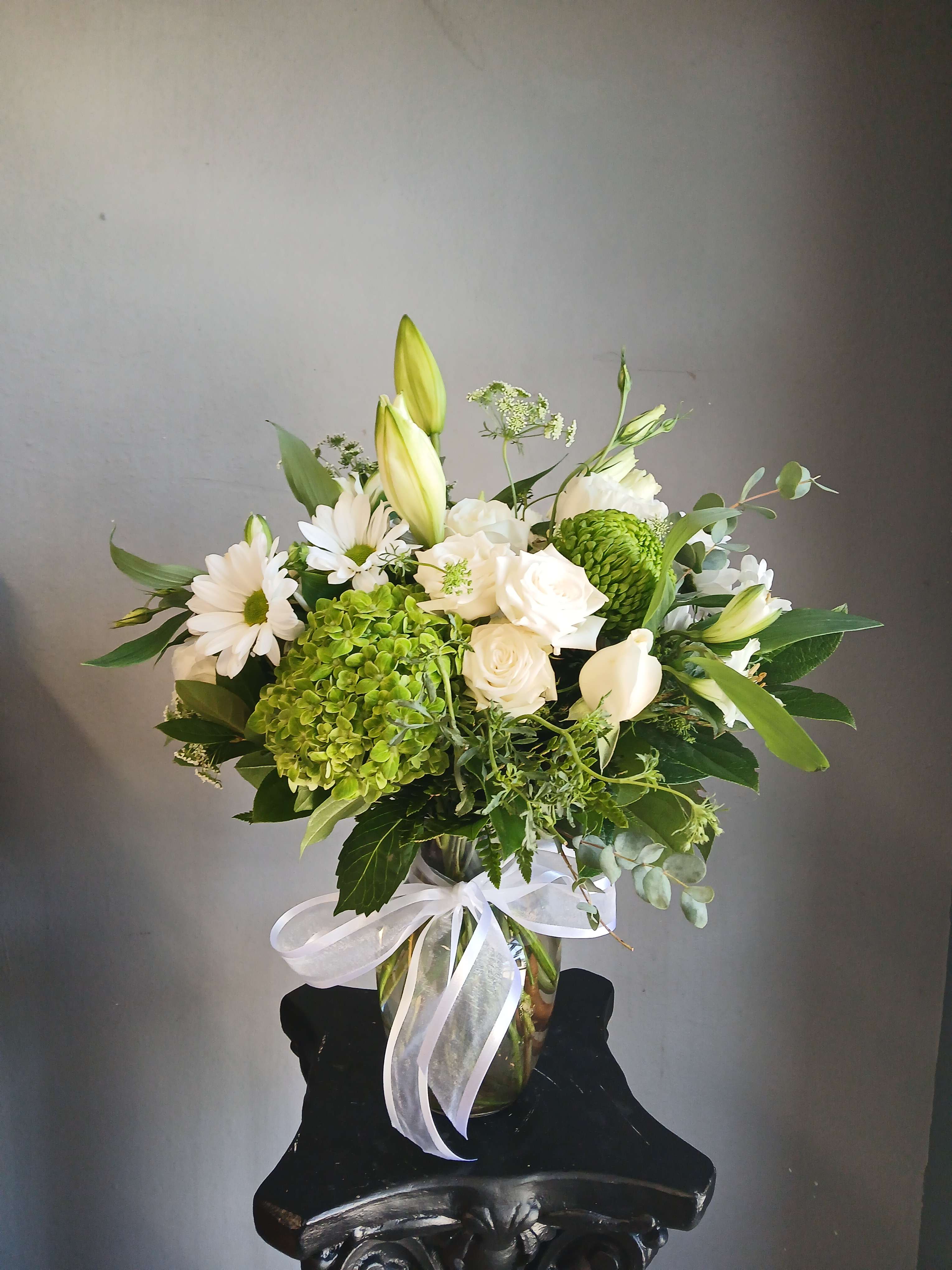 White and green floral arrangement in a glass vase with a white ribbon