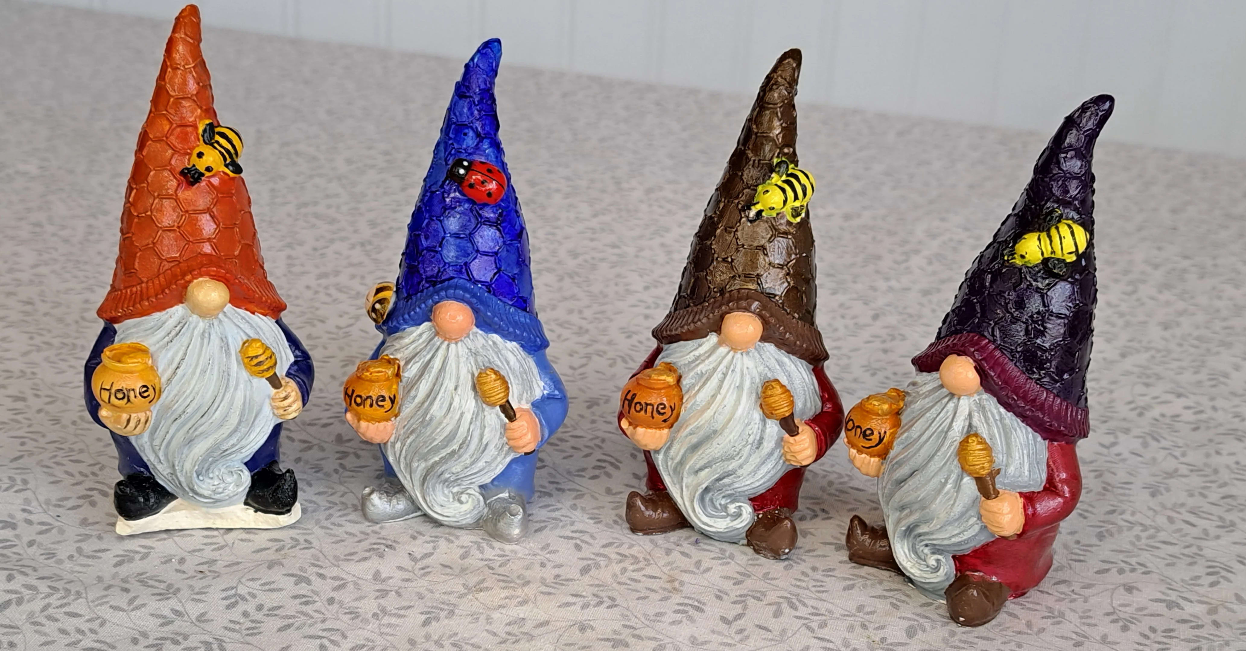 Set of four colorful gnome figurines holding honey pots with bees and a ladybug on their tall textured hats.