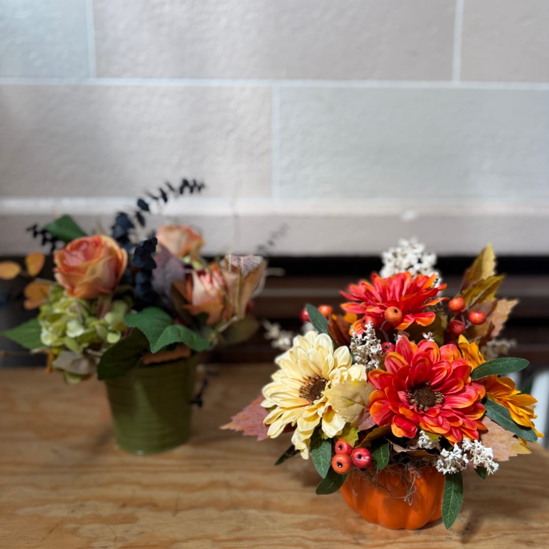 Two autumn floral arrangements in small containers, one in a pumpkin vase
