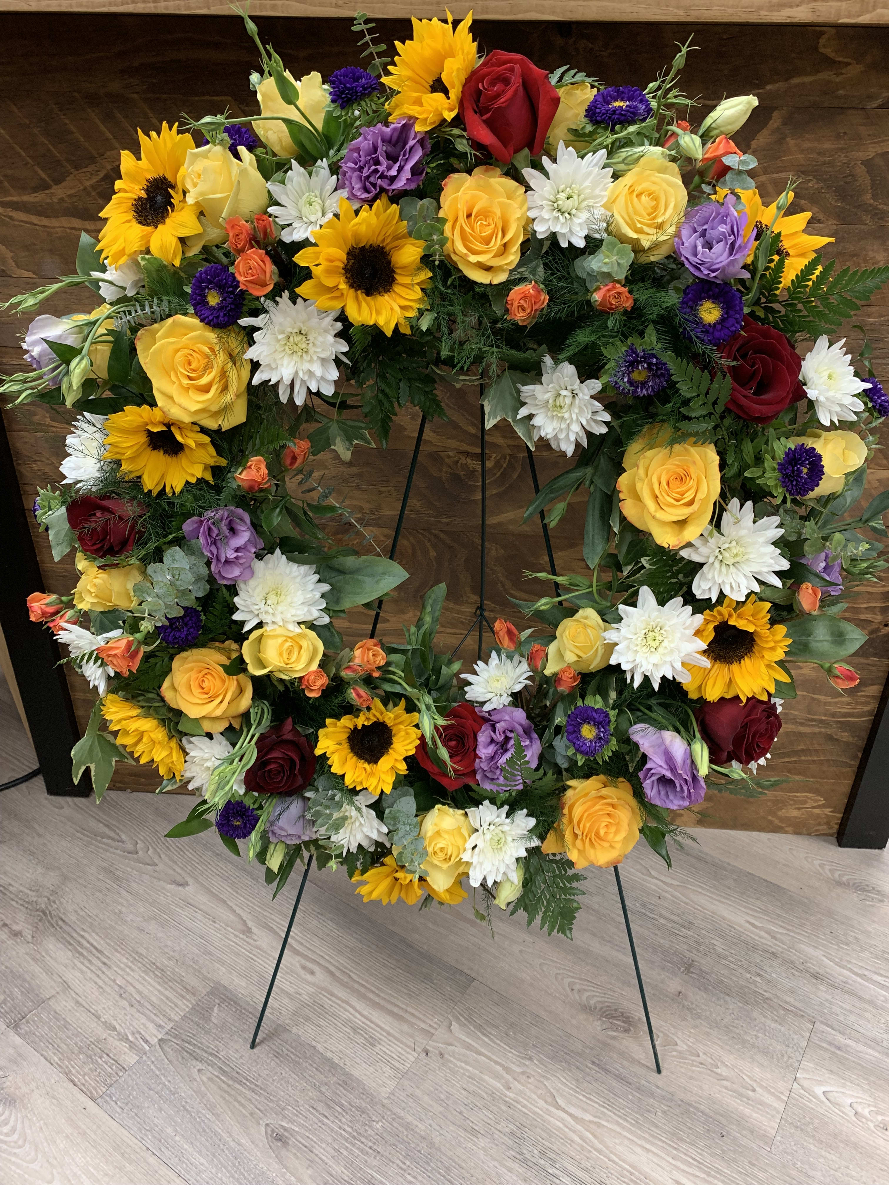 Heart-shaped floral wreath with roses, sunflowers, and white daisies on a stand