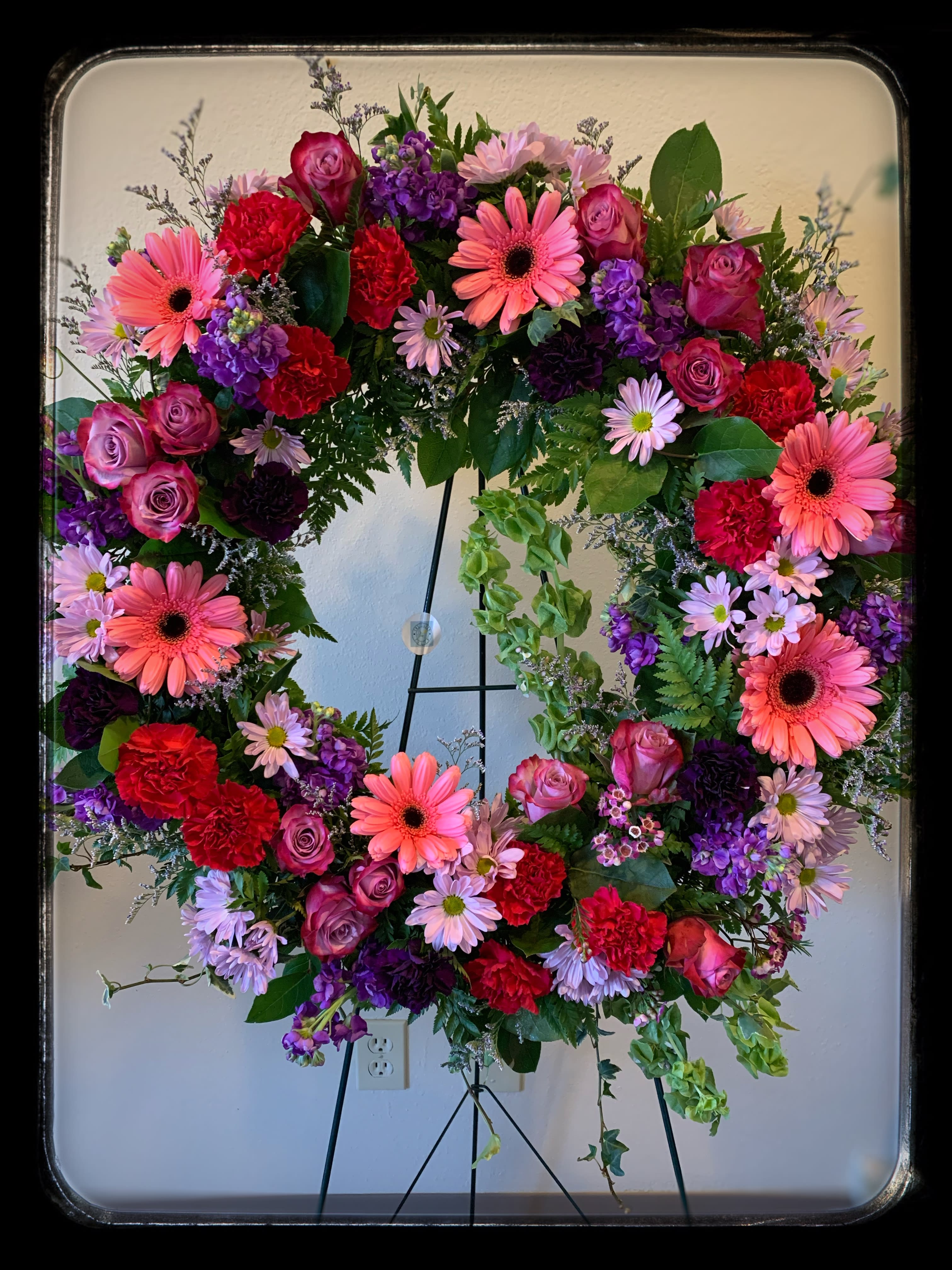 Large floral wreath with pink, purple, and red blooms on a stand