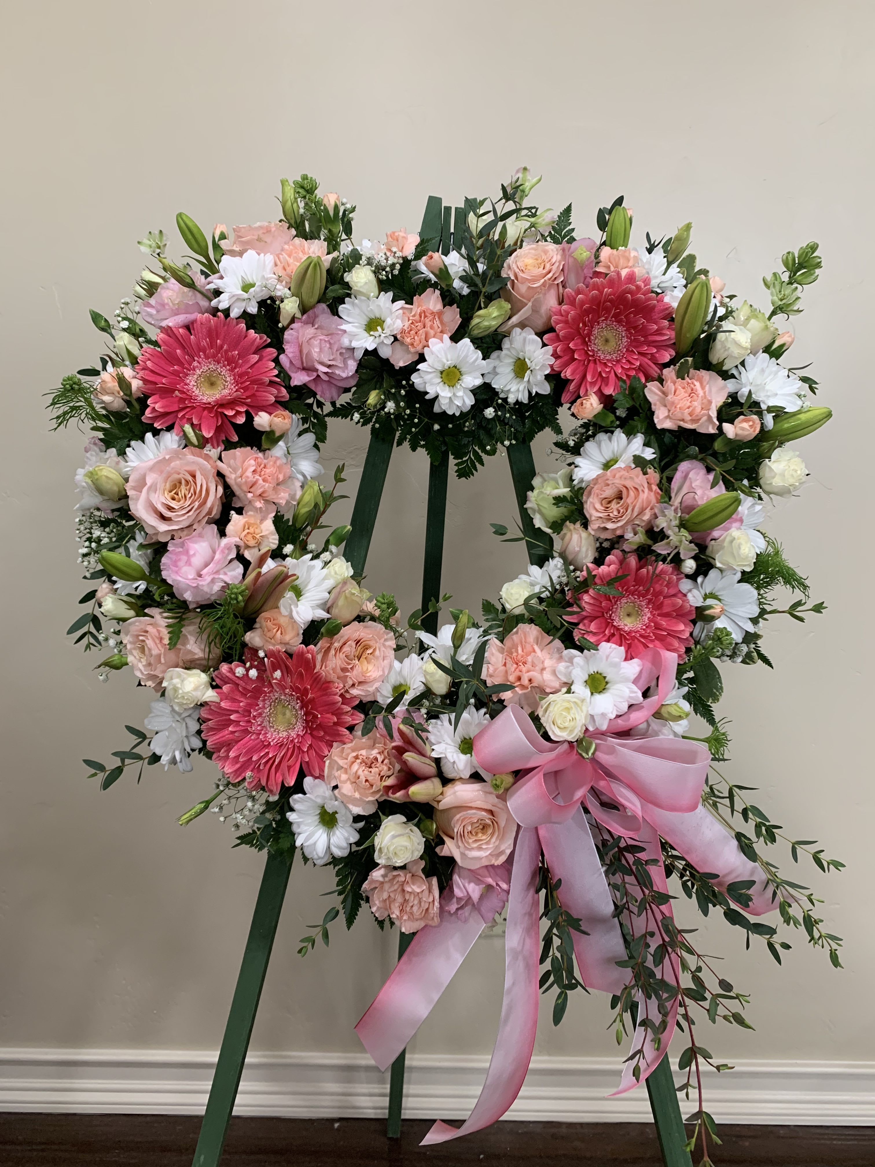 Heart-shaped floral wreath on a stand with pink and white flowers and a pink ribbon