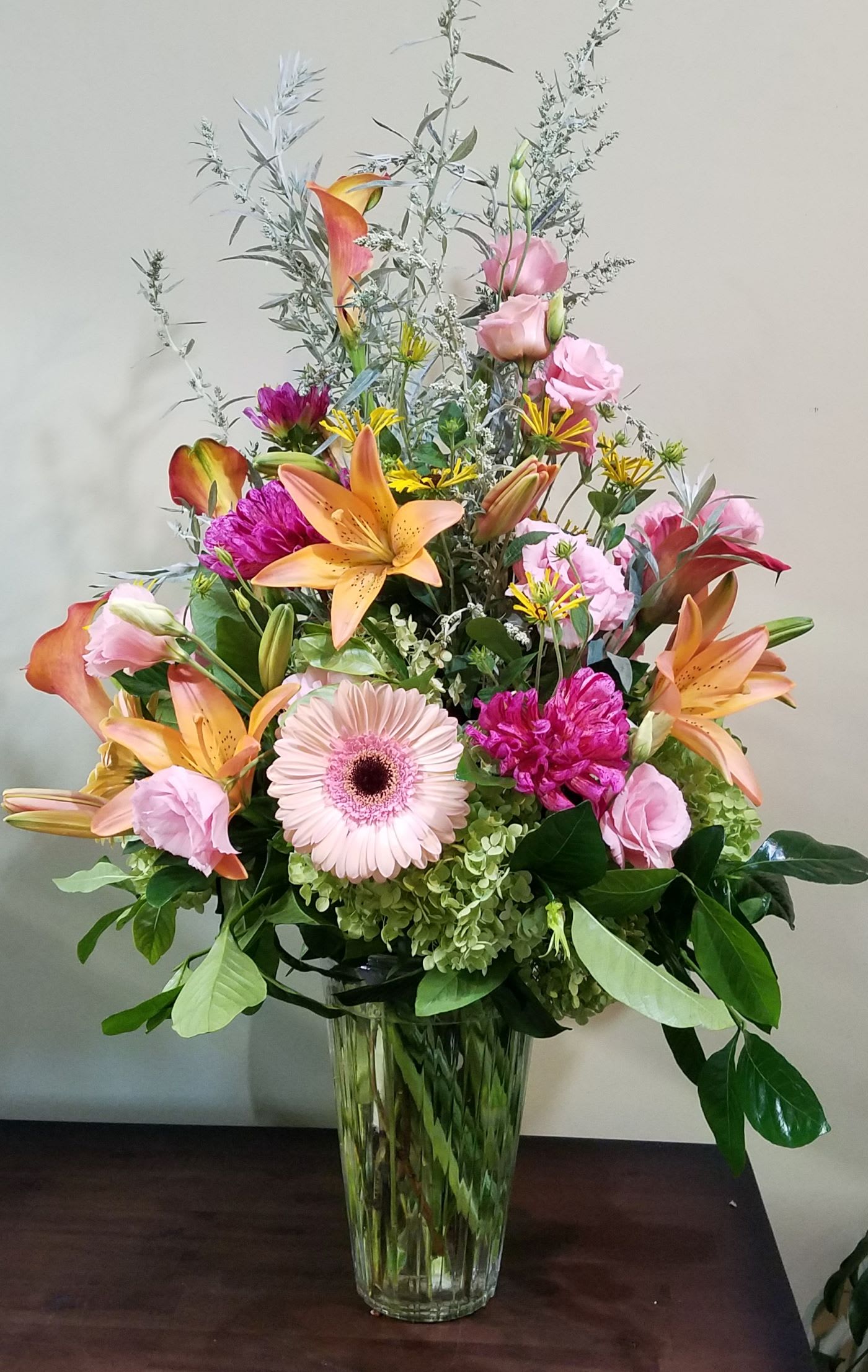 Tall mixed bouquet of lilies, gerbera, hydrangea, and calla lilies in a clear glass vase