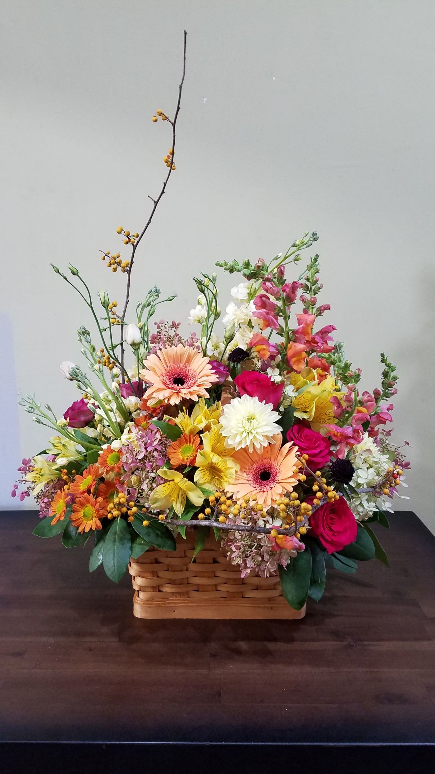 Colorful mixed flower basket with gerbera daisies, roses, snapdragons, and mums in warm tones.