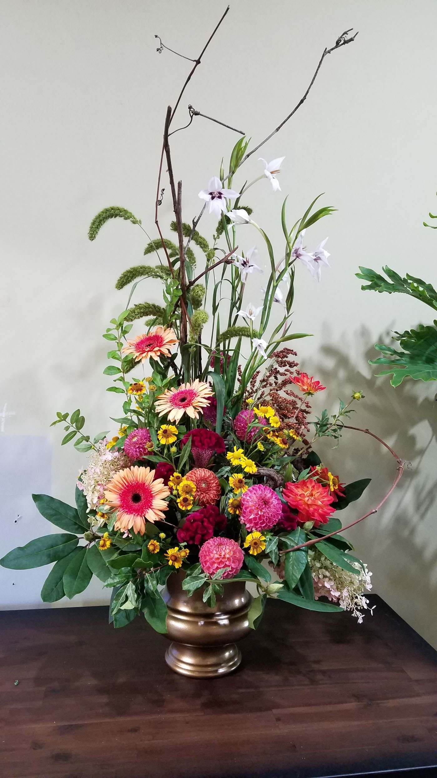 Tall mixed arrangement of pink and orange blooms with yellow accents in a gold pedestal vase