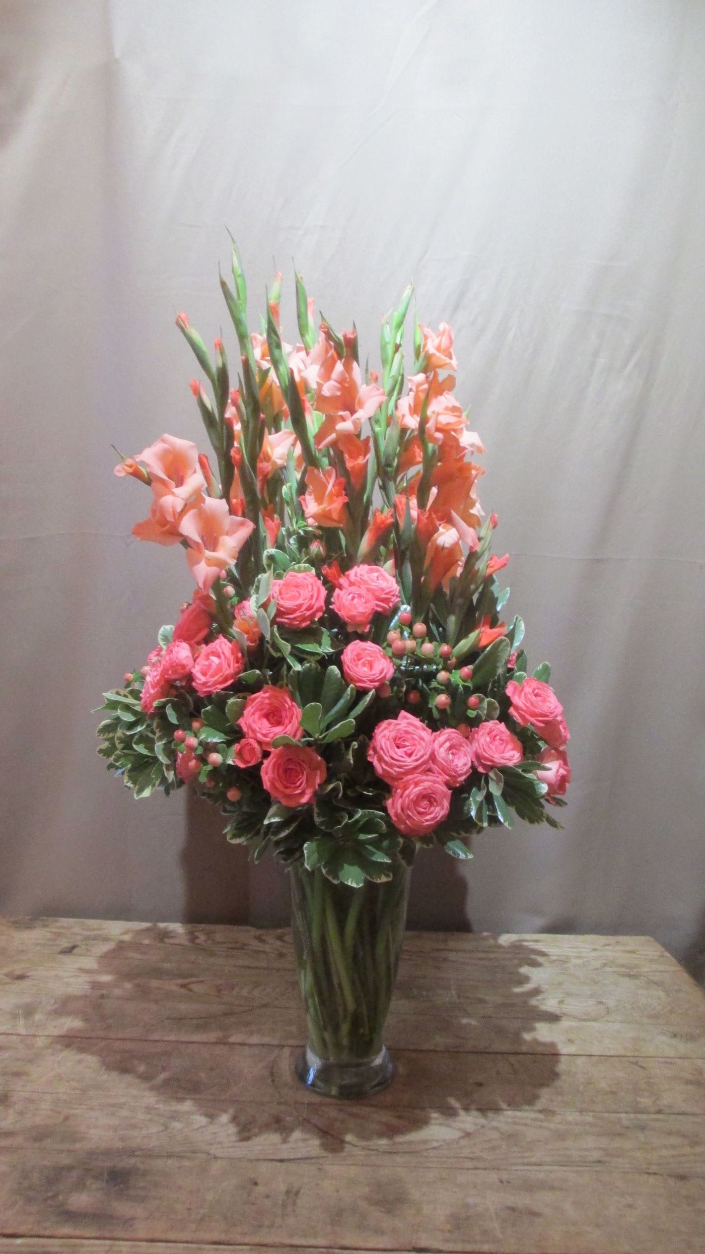 Tall arrangement of peach gladiolus and bright pink spray roses in a clear glass vase
