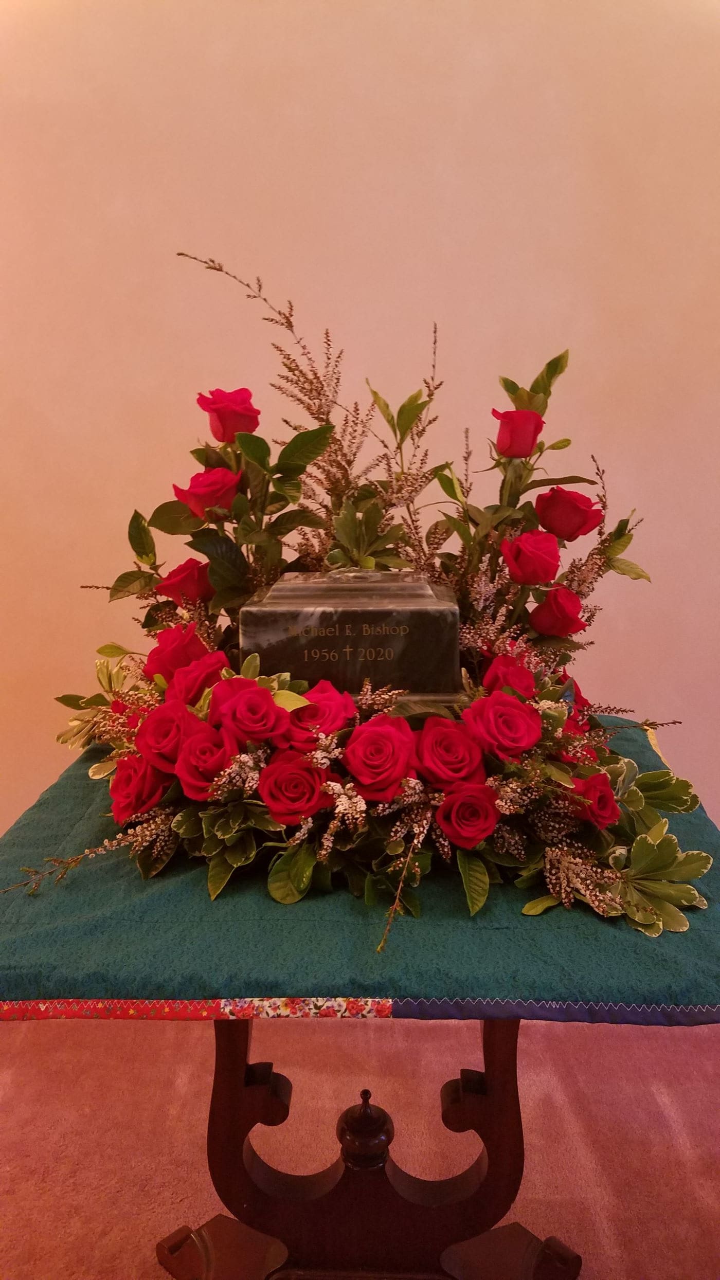 Red rose cremation wreath surrounding a dark urn on a teal-covered table