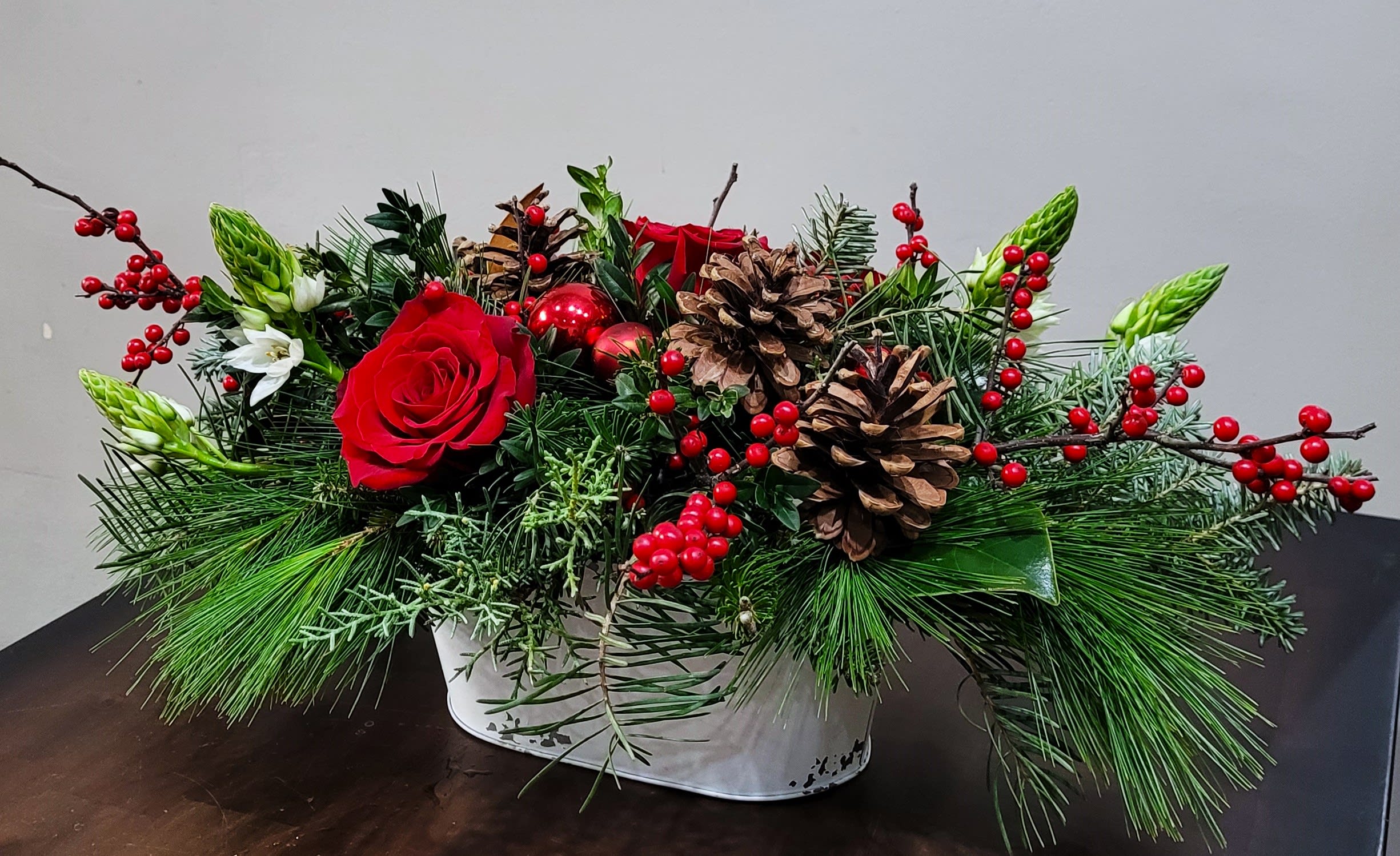 Low Christmas centerpiece with red roses, red berries, pinecones, and evergreen in a white container