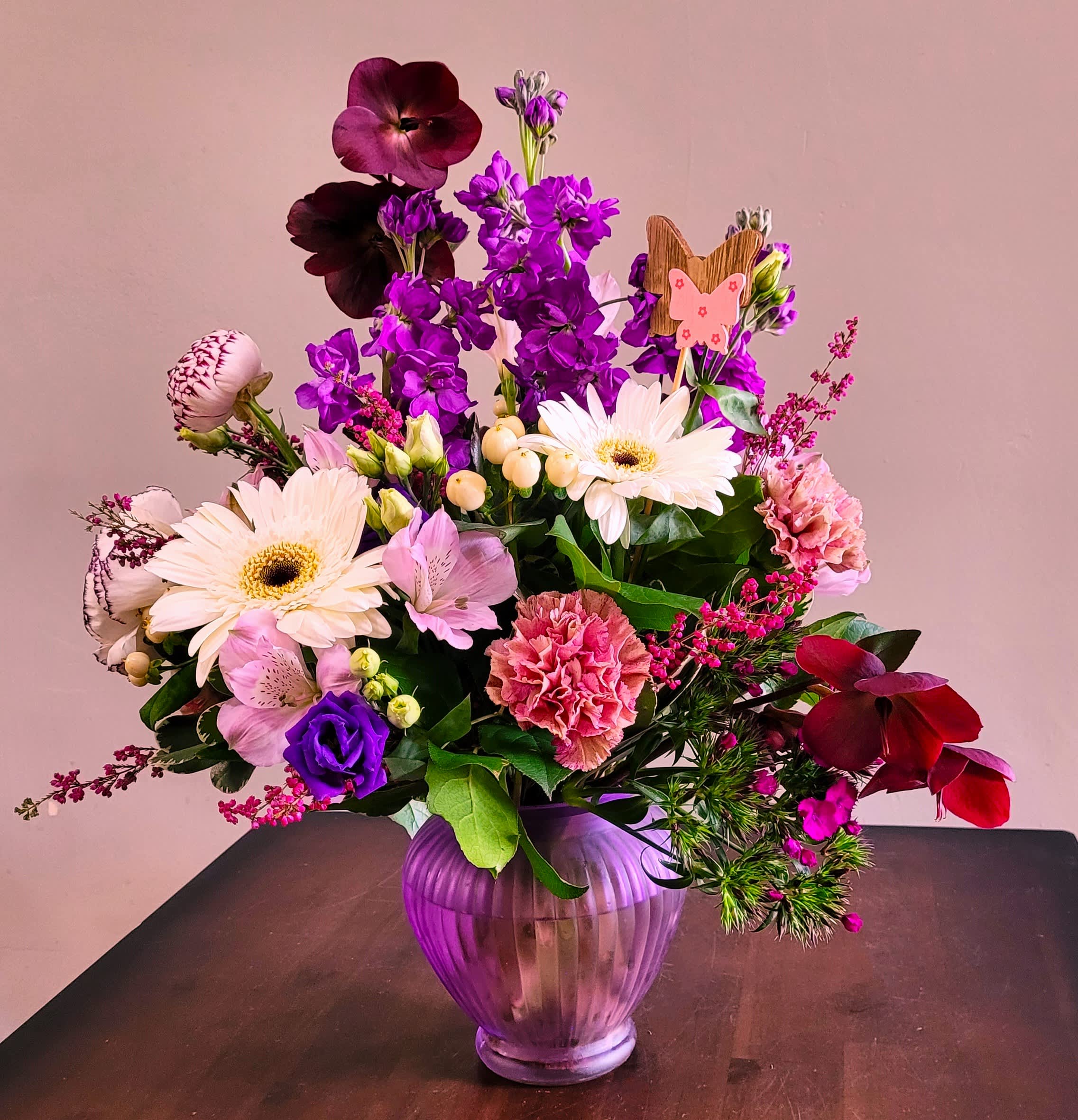 Mixed pink, purple, and white flower arrangement in a purple glass vase with a small butterfly pick