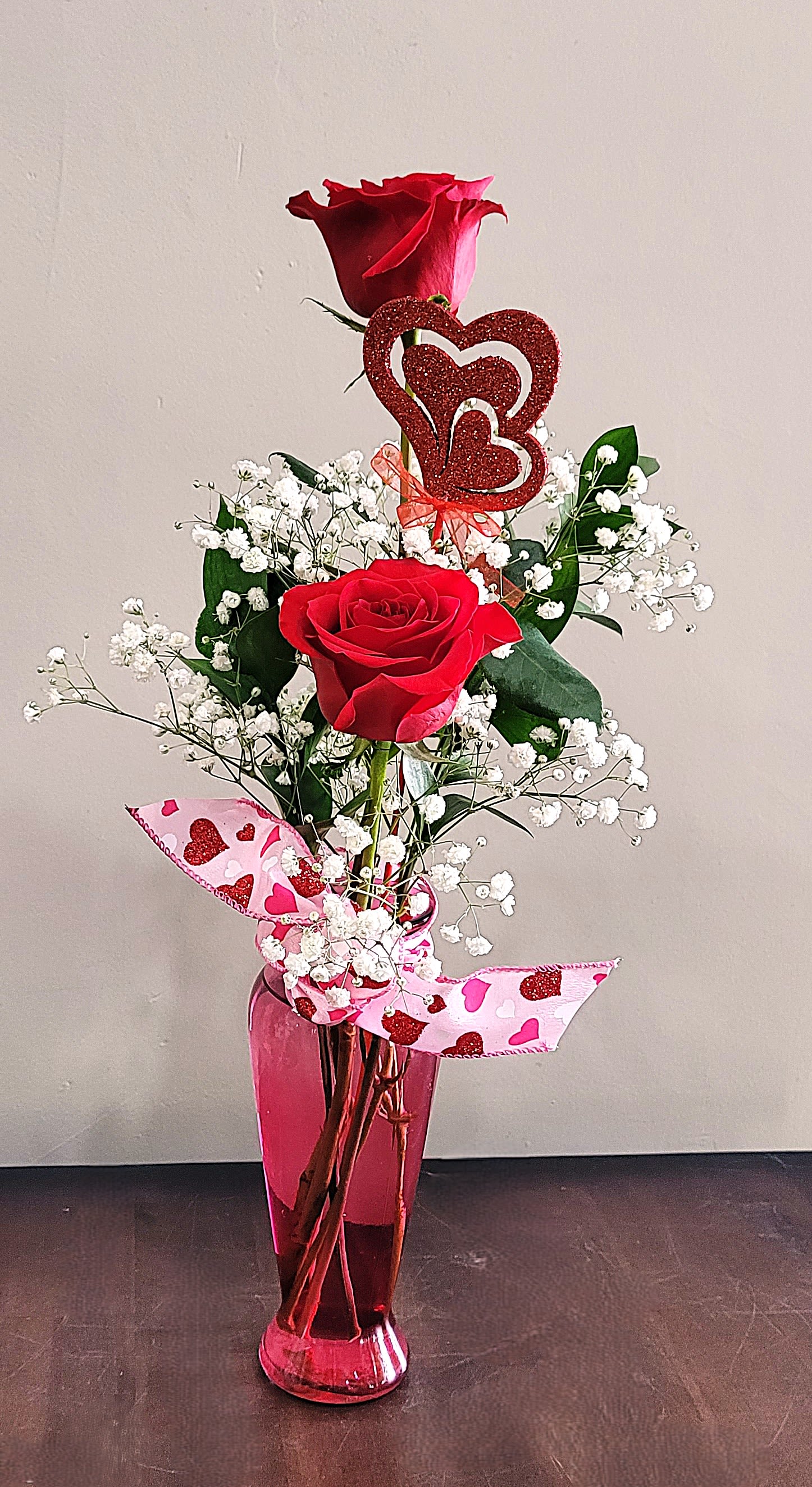 Tall pink vase with two red roses, baby’s breath, and a glitter heart pick