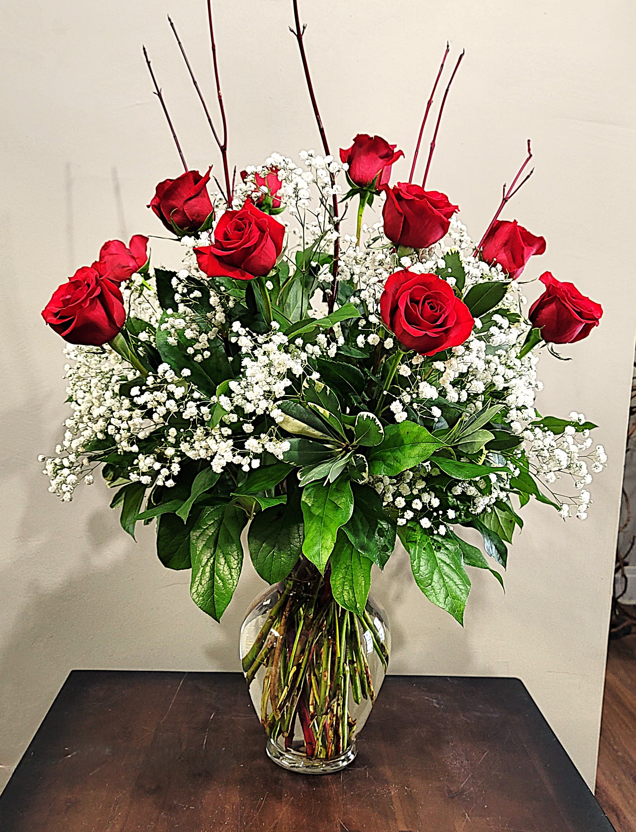 Tall arrangement of red roses and white filler flowers in a clear glass vase on a dark table