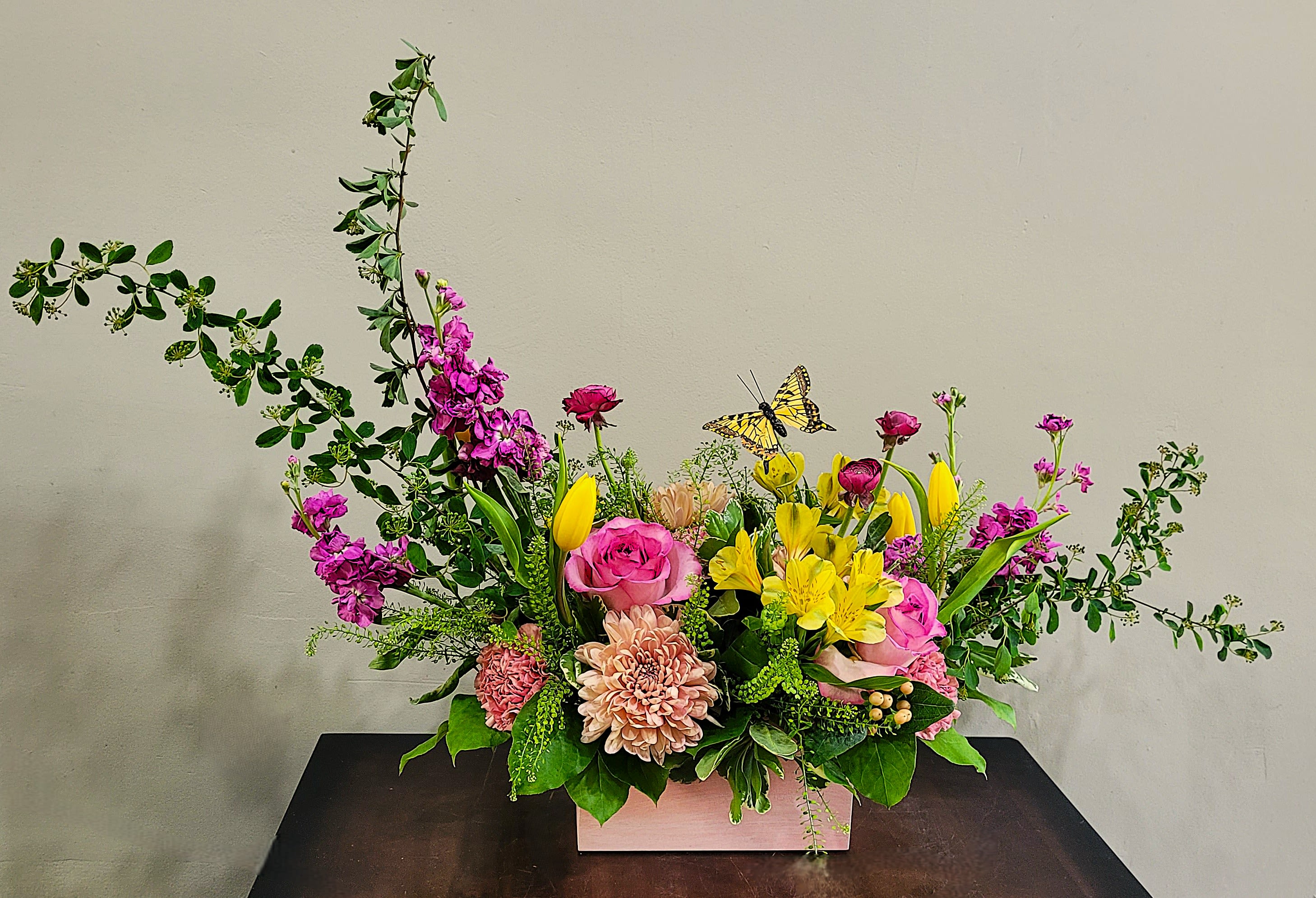 Butterfly Box in Pink  - A contemporary crescent design in a pastel washed wooden box filled with soft spring colors of roses, large Disbud Cremons, Stock, Ranunculus, Tulips with accents of fresh blossom greens.