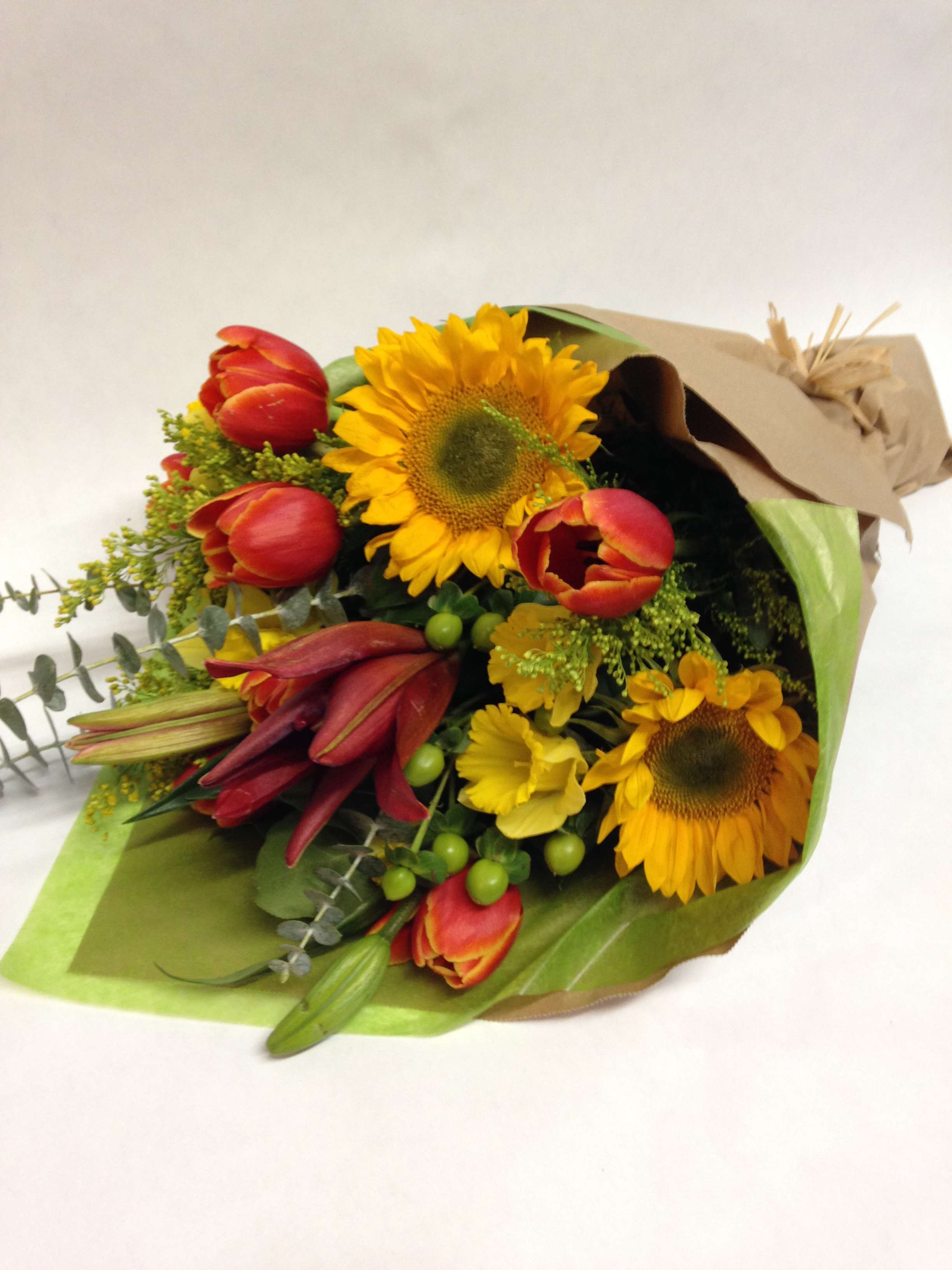 Bouquet of sunflowers, red tulips, and yellow lilies wrapped in paper