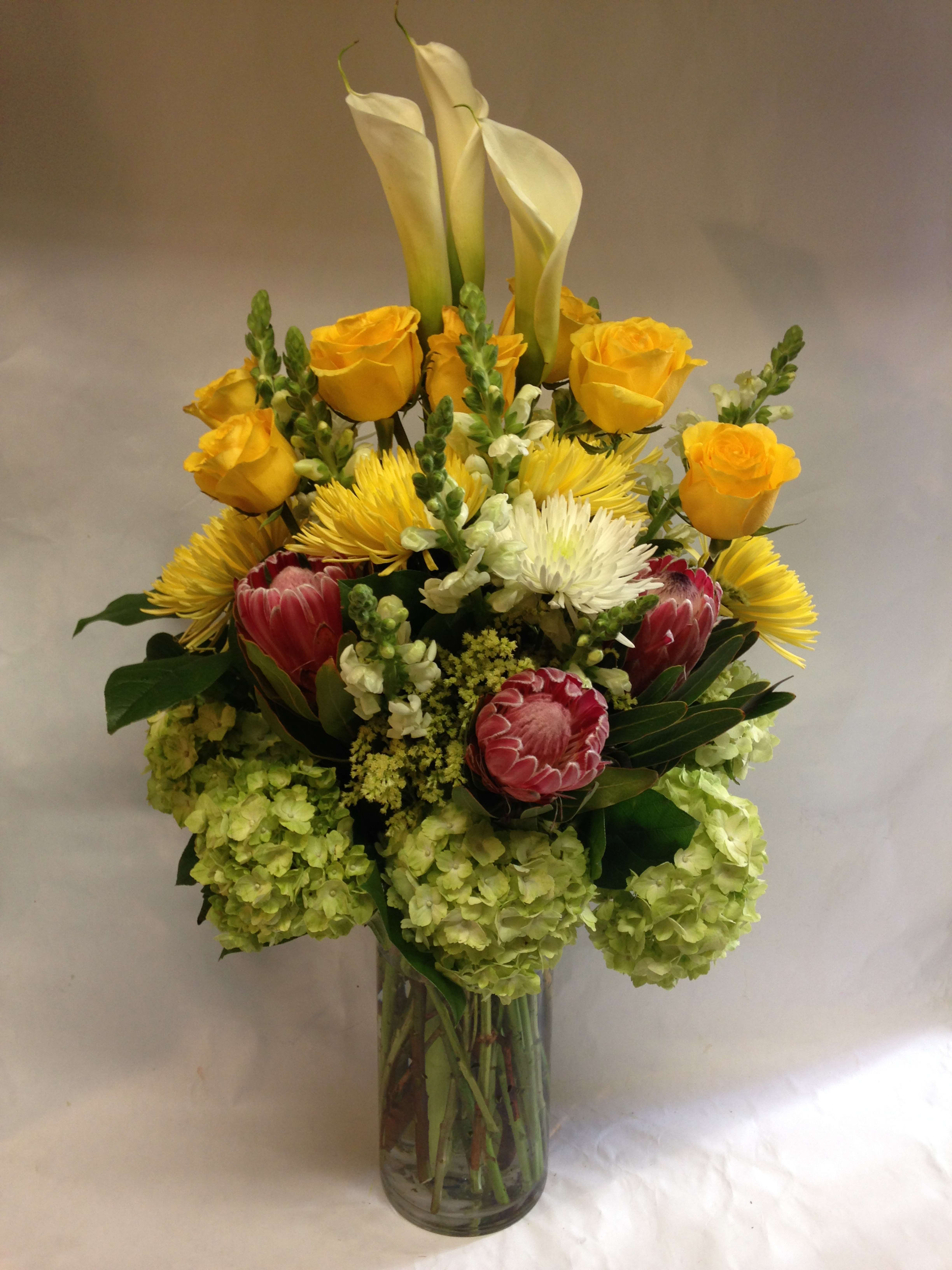 Mixed bouquet with yellow roses, white calla lilies, and pink protea in a glass vase