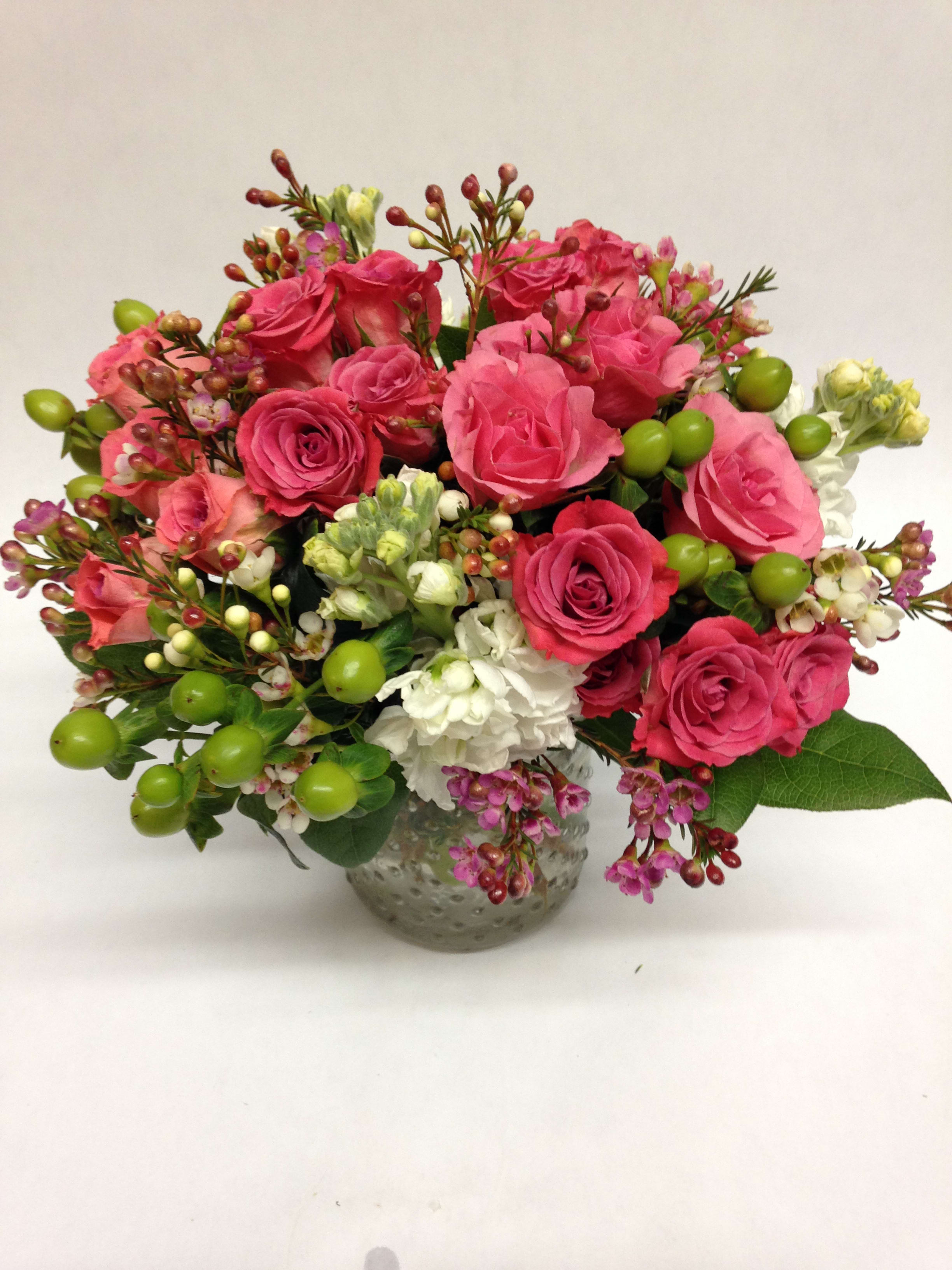 Pink rose bouquet in a textured glass vase with white blooms and green berries