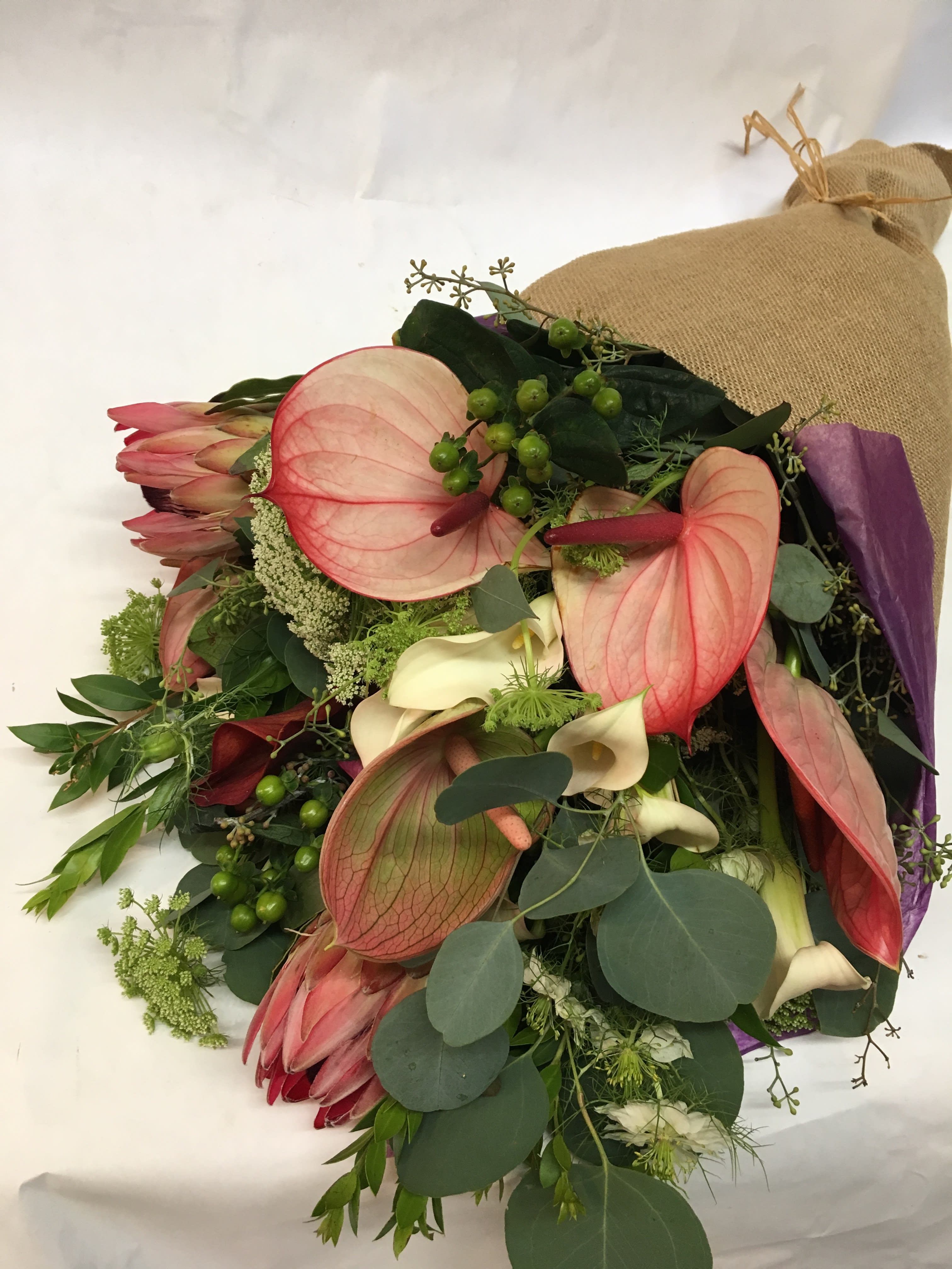 Bouquet with pink anthuriums, cream calla lilies, and dark greenery wrapped in burlap