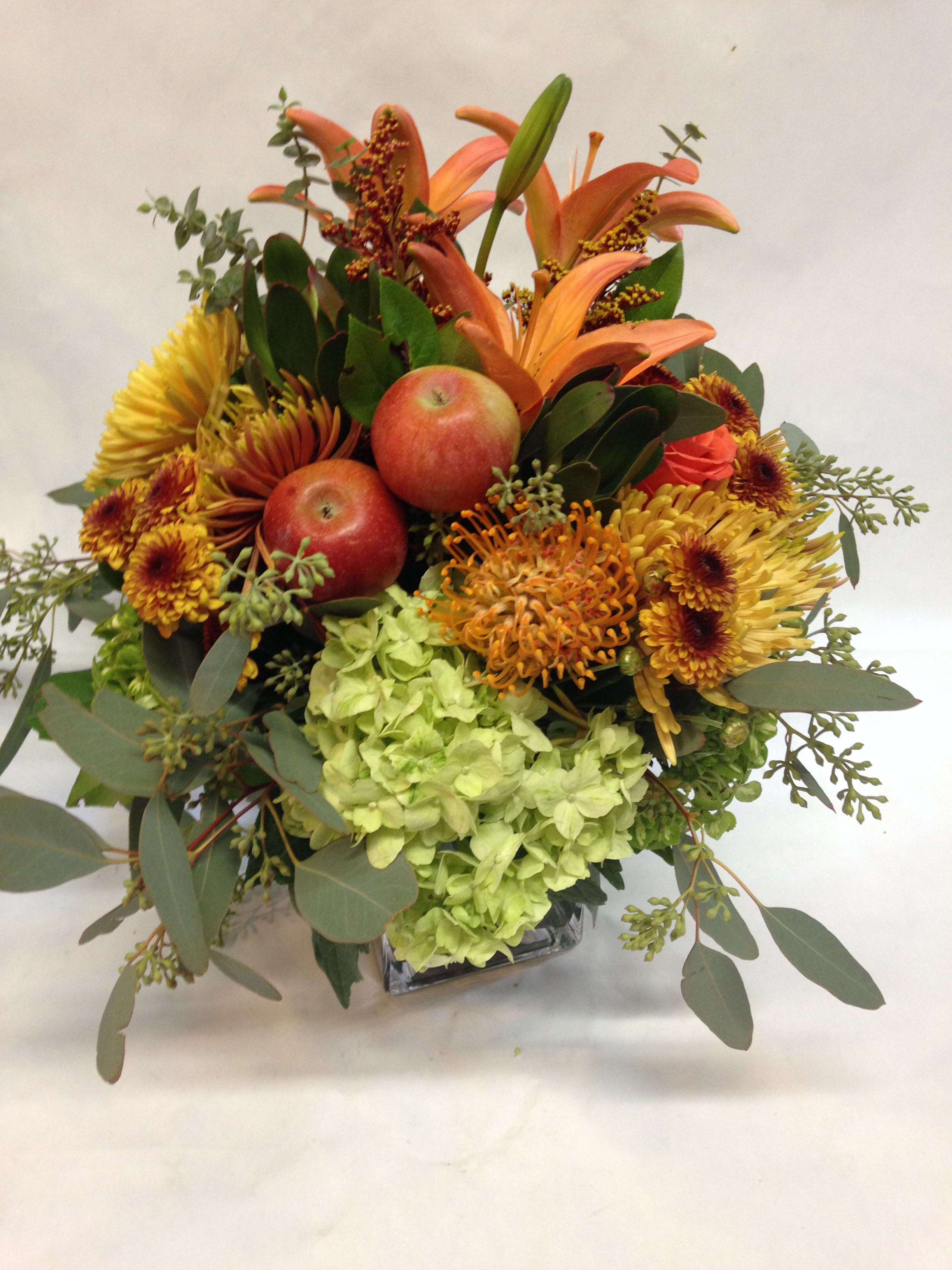 Orange lilies and chrysanthemums with apples in a glass vase