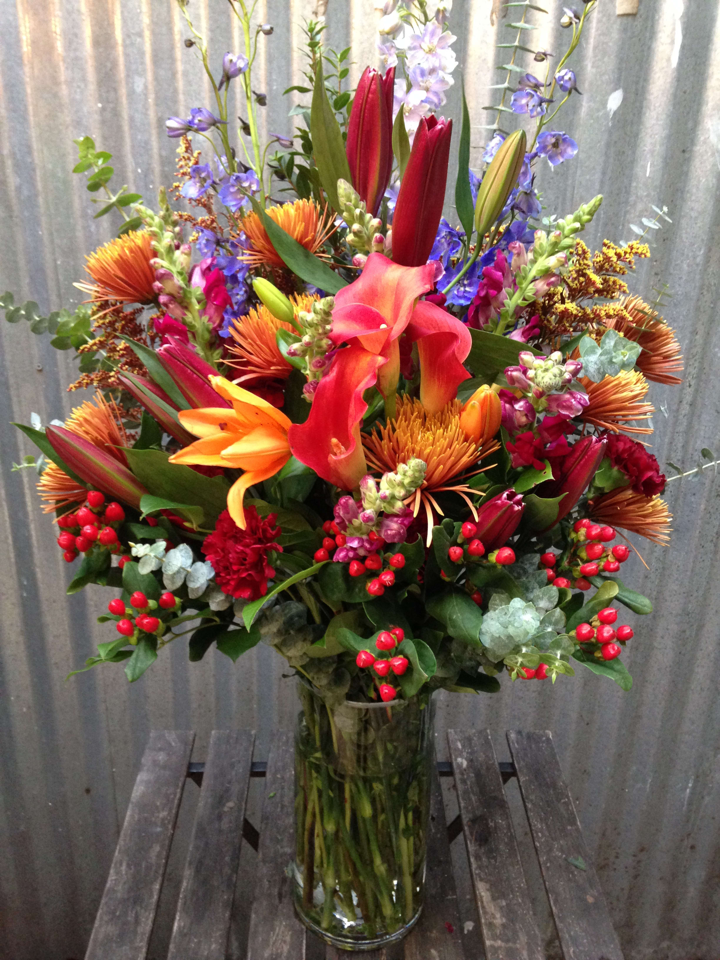 Tall mixed bouquet with lilies, calla lilies, and orange blooms in a glass vase