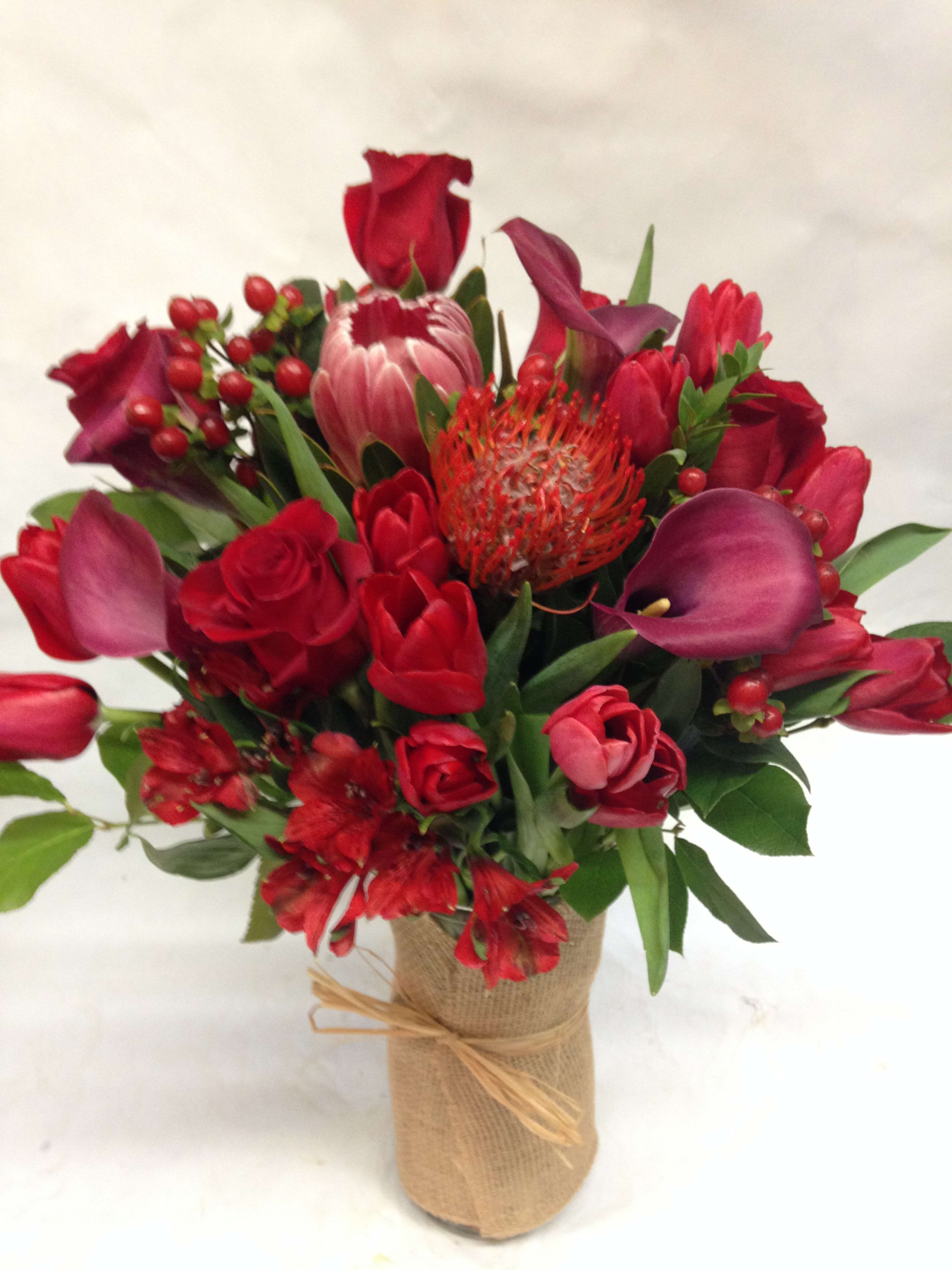 Red floral bouquet with roses, tulips, and calla lilies in a burlap-wrapped vase