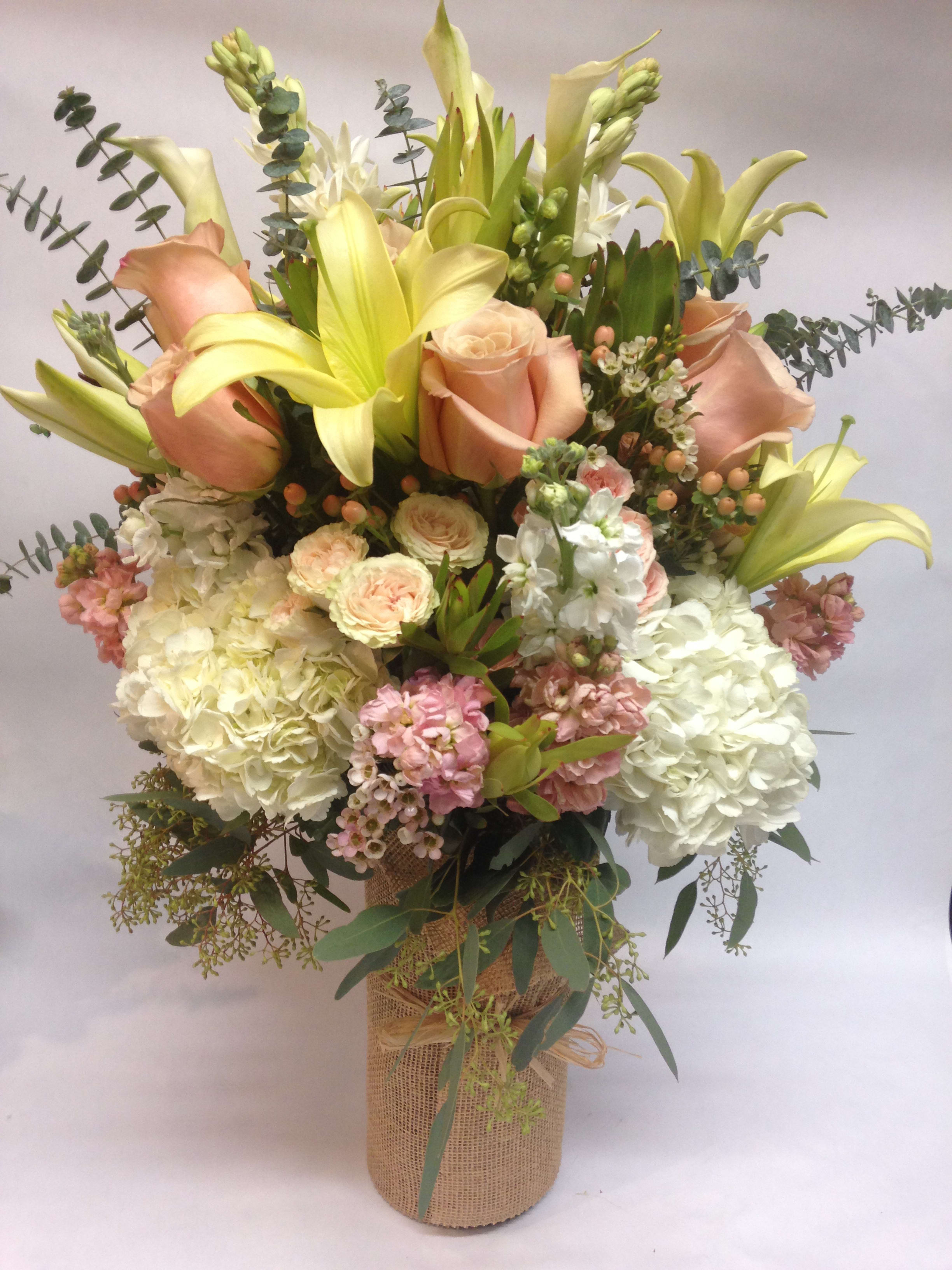 Bouquet of peach roses, yellow lilies, and white hydrangeas in a burlap-wrapped vase