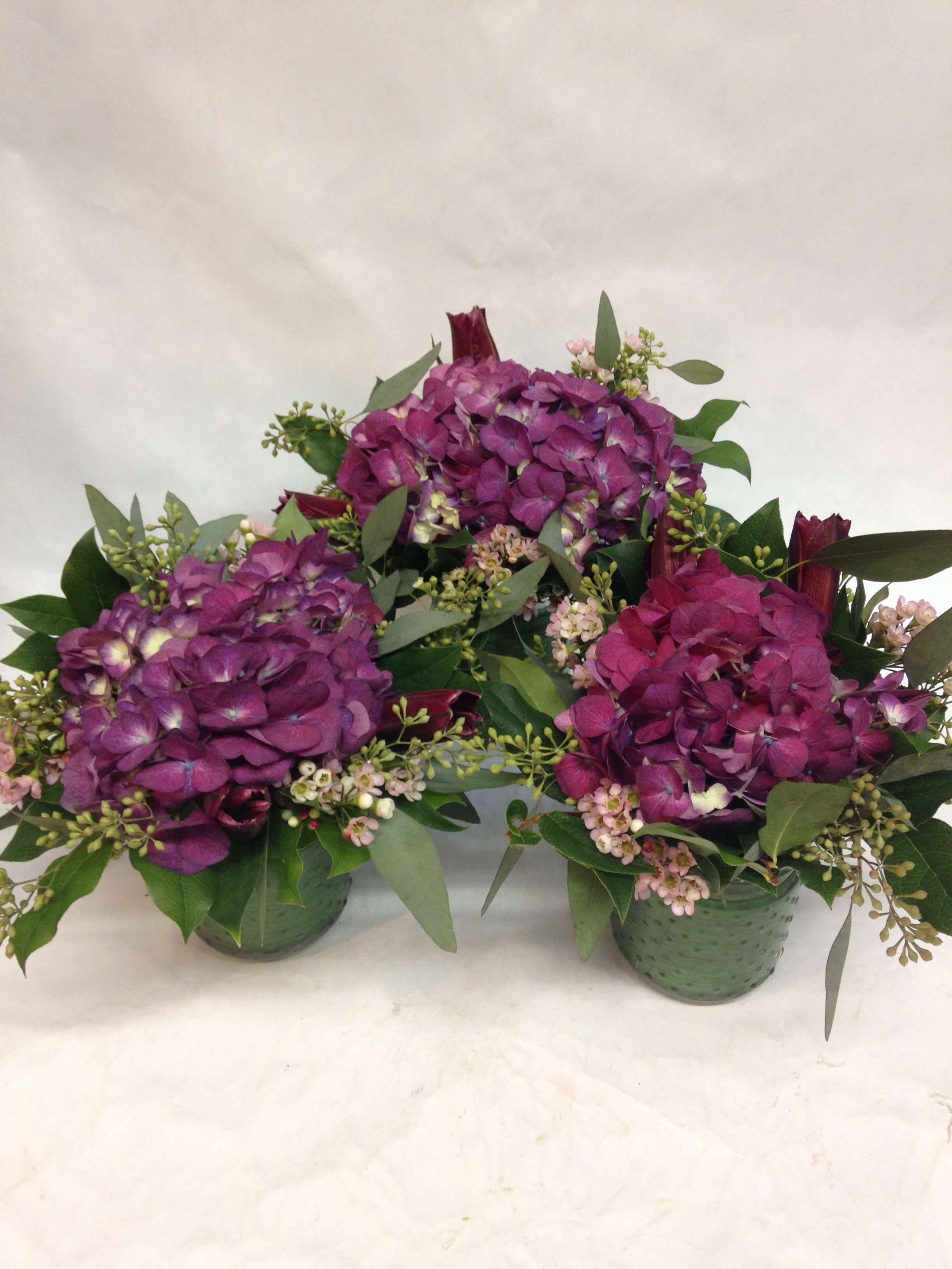 Three purple hydrangea arrangements in green containers