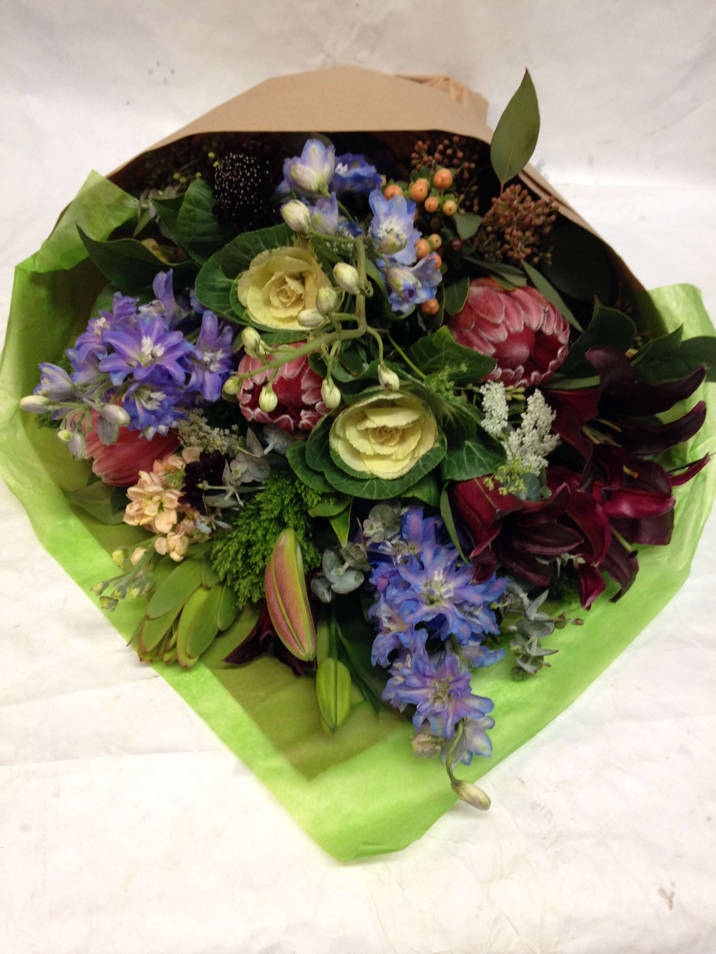 Mixed bouquet with purple, pink, and cream flowers wrapped in green paper