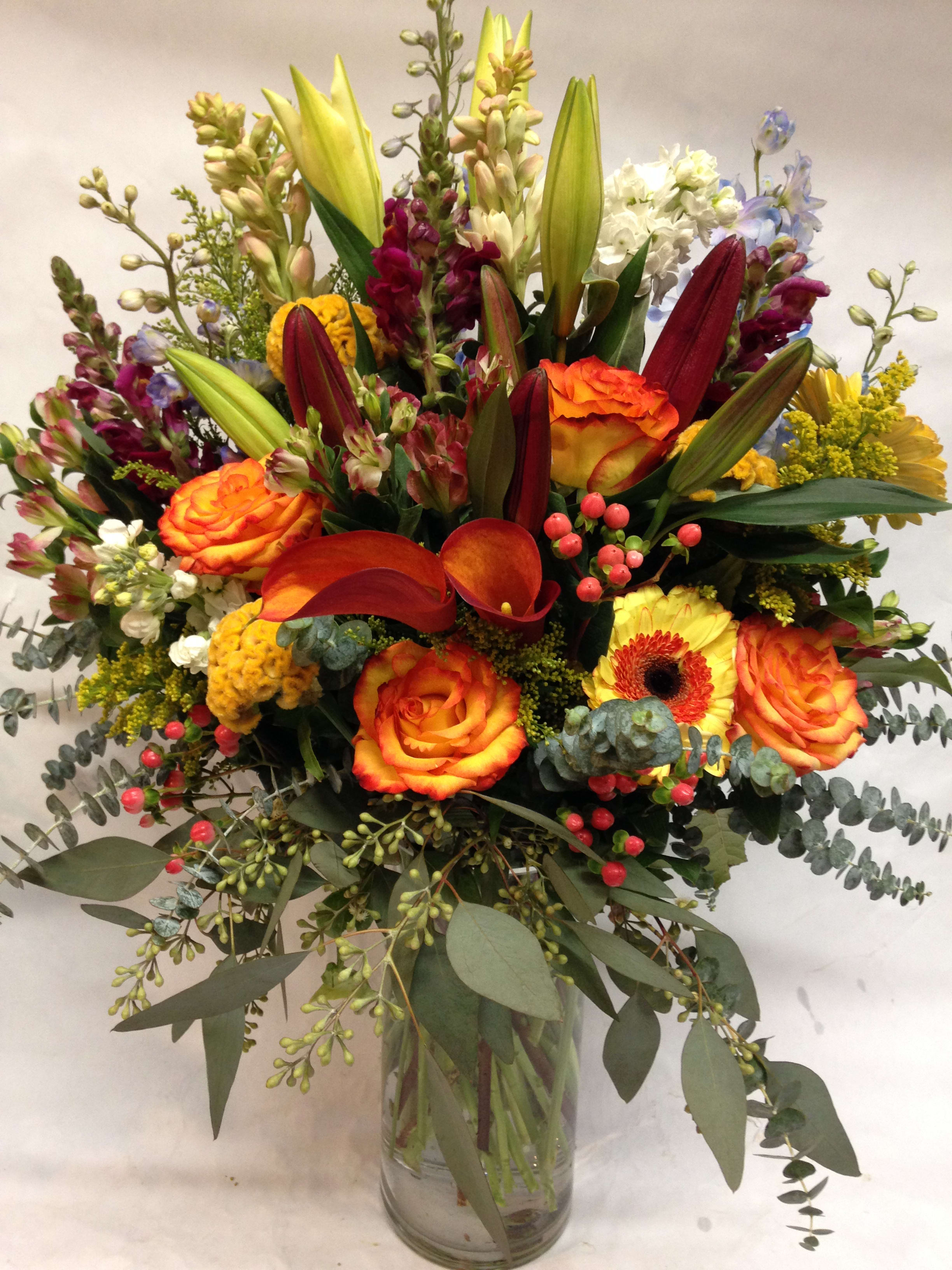 Mixed bouquet of orange roses, lilies, and calla lilies in a glass vase