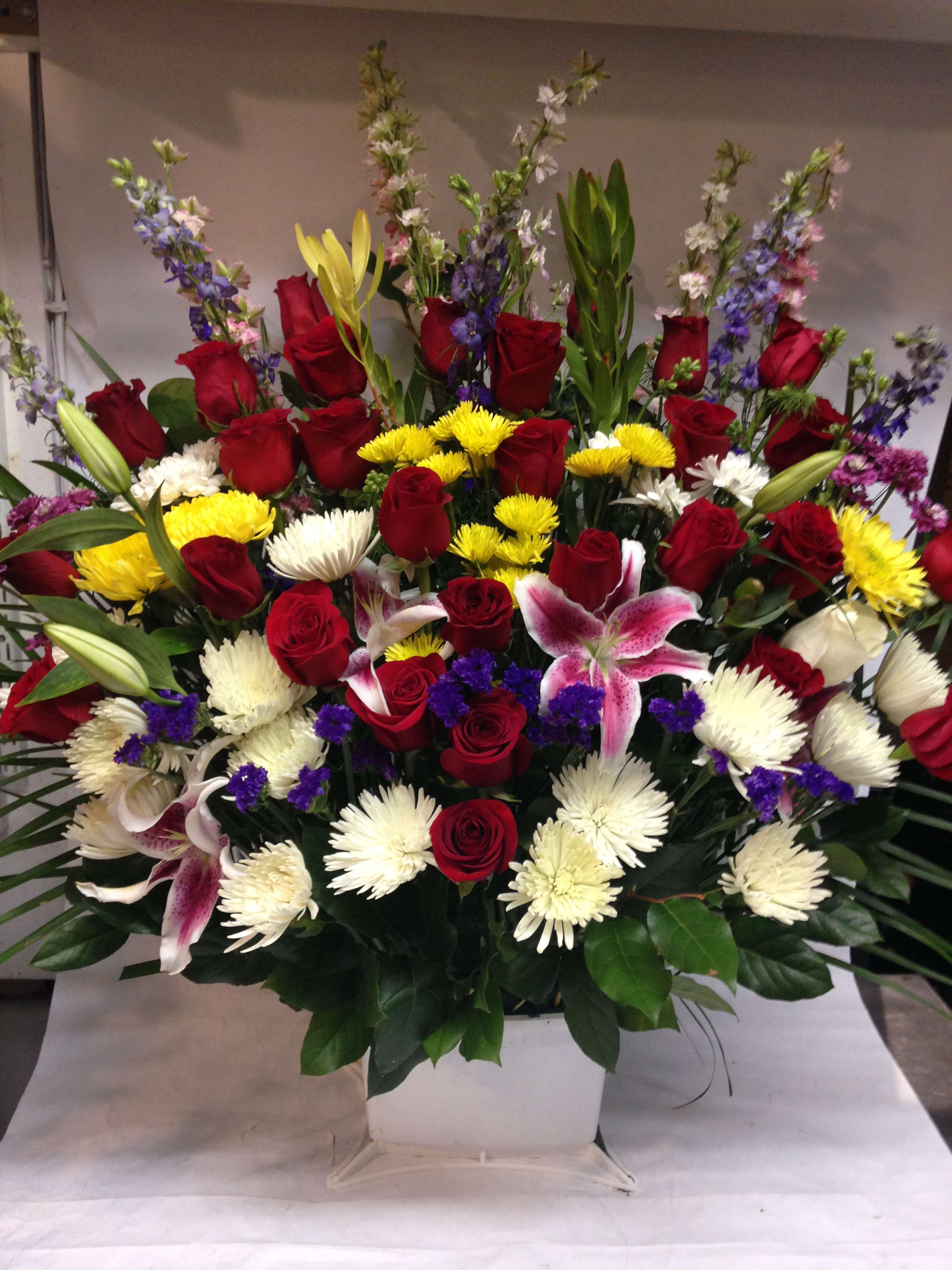 Large mixed bouquet of red roses, lilies, and white chrysanthemums in a white container