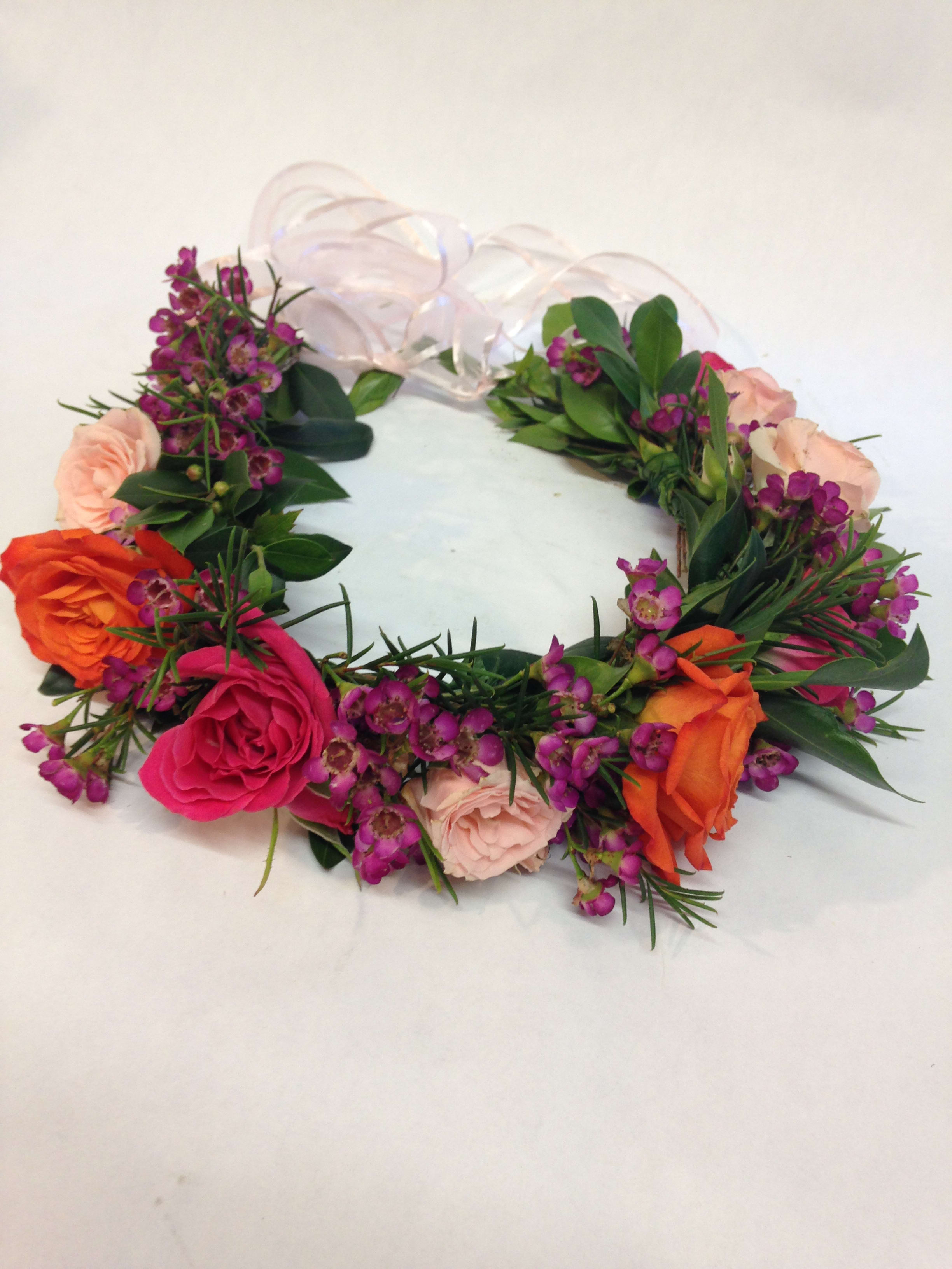 Floral wreath with pink, orange, and purple blooms on a white ribbon base