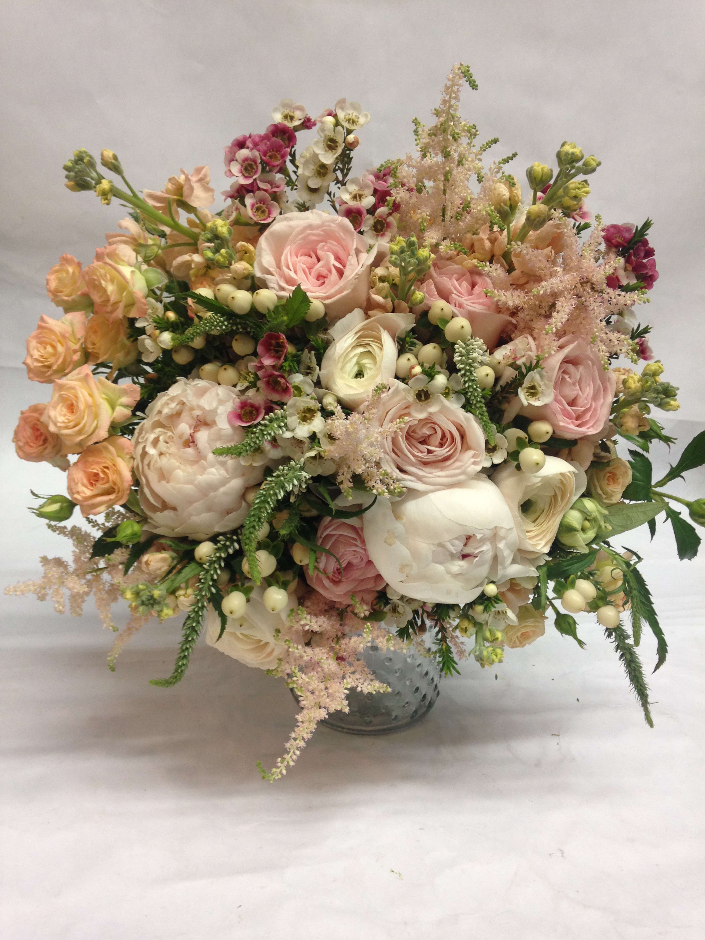 Blush and cream bouquet of roses, peonies, and small filler flowers in a glass vase.