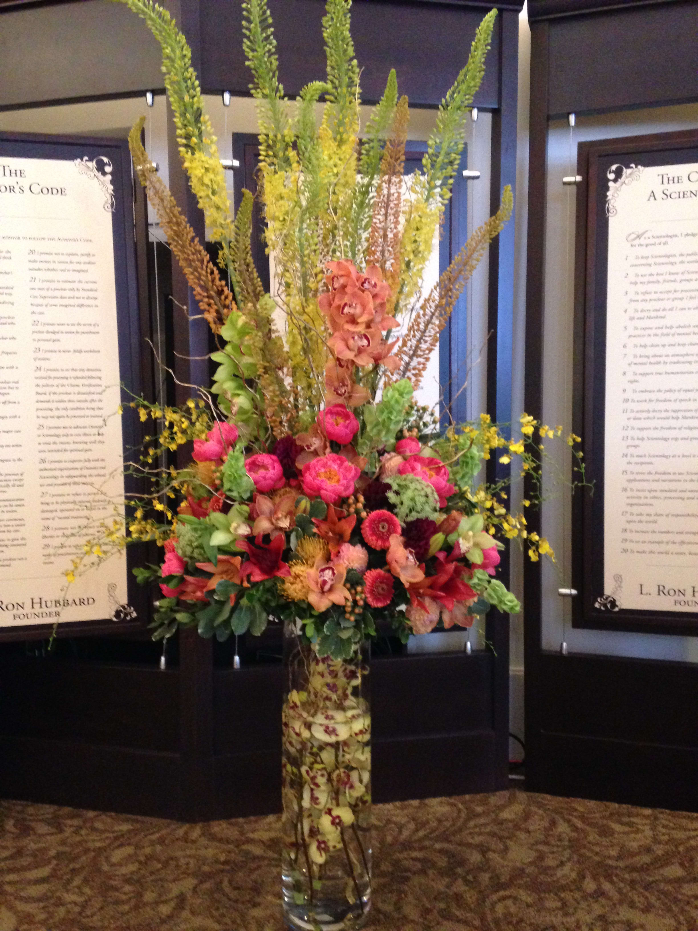 Tall mixed floral arrangement in a clear glass vase with pink and orange blooms