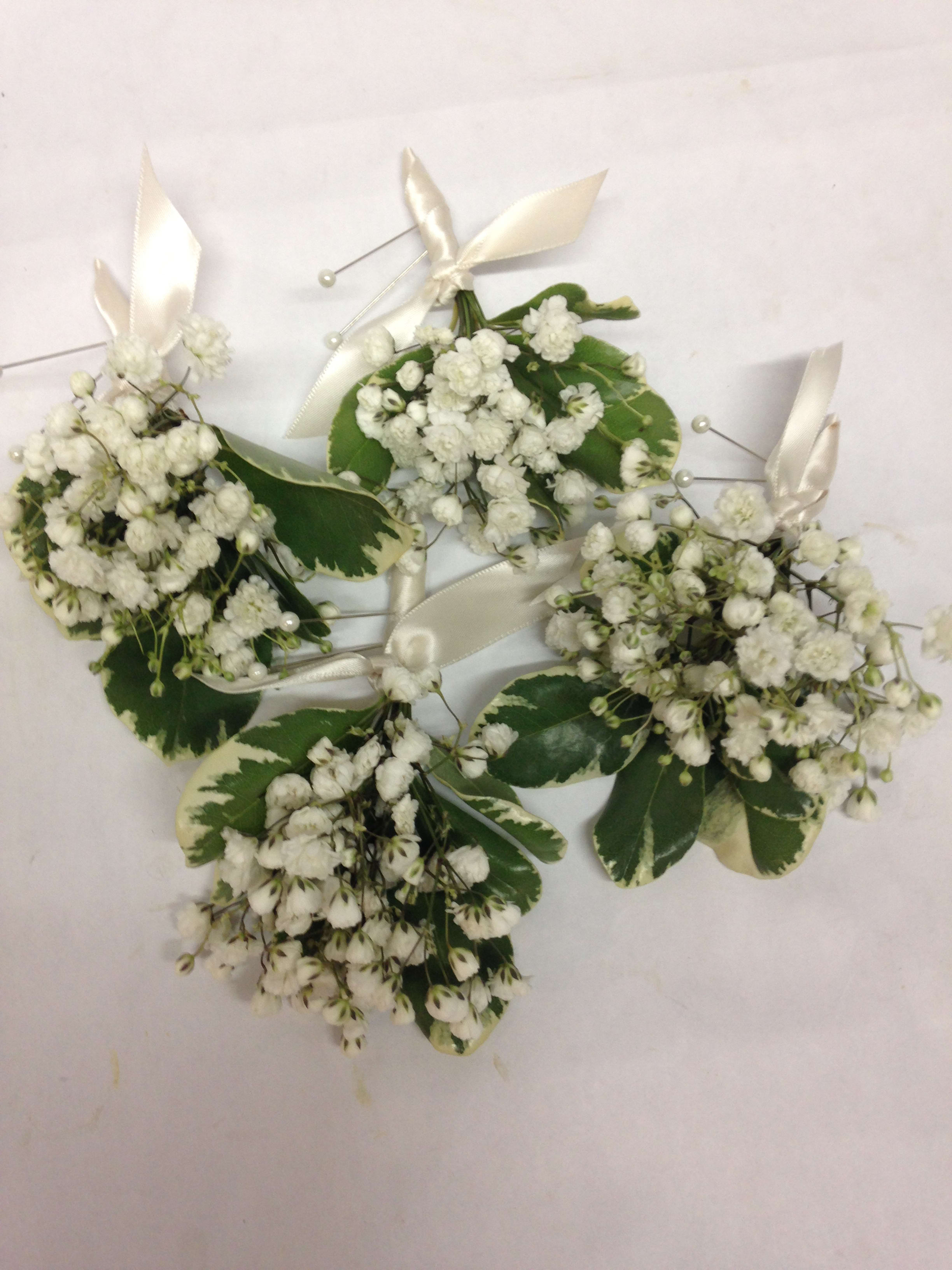 White baby’s breath corsages with cream ribbon and variegated leaves