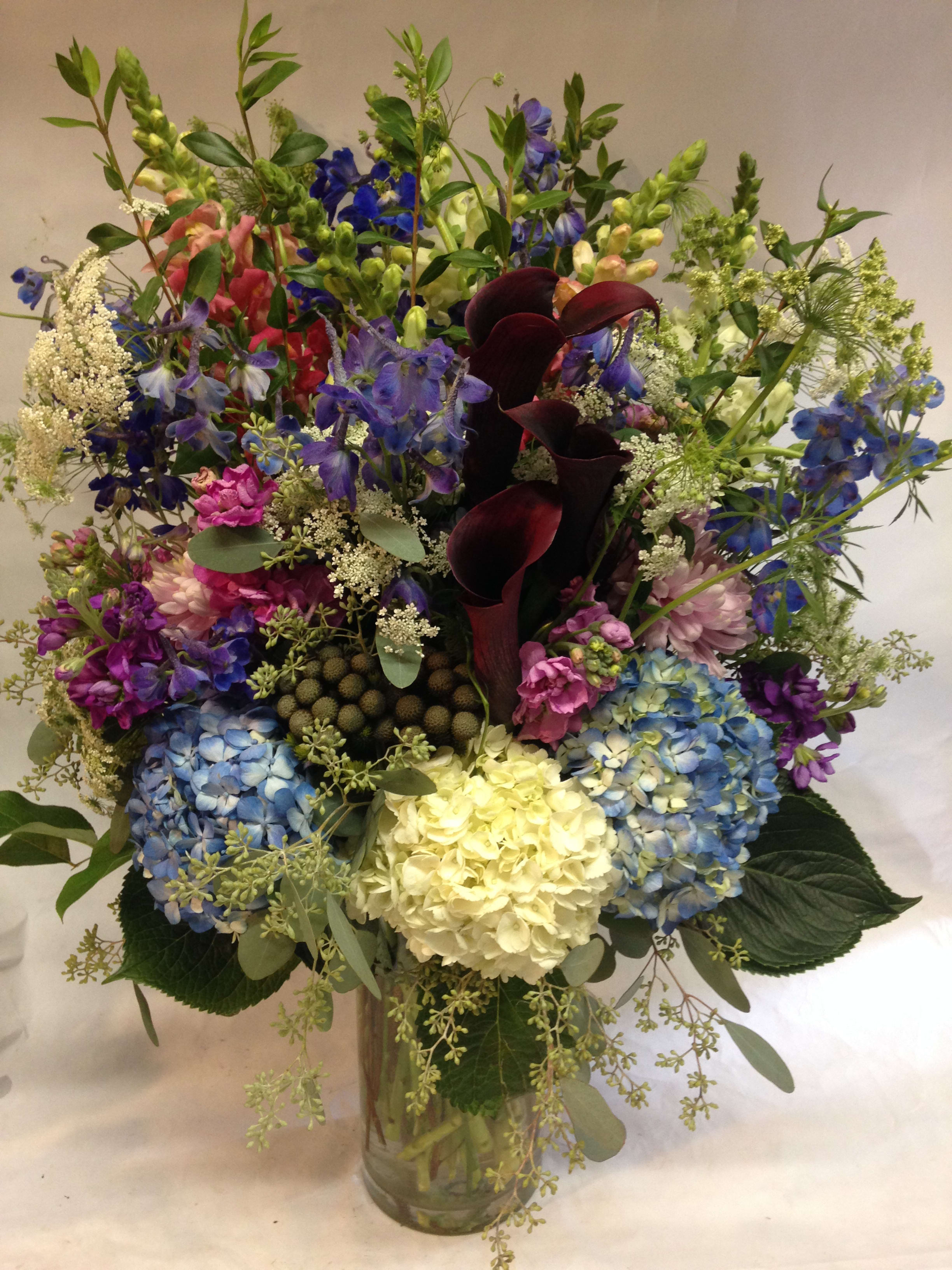 Mixed bouquet with hydrangeas, calla lilies, and delphinium in a glass vase