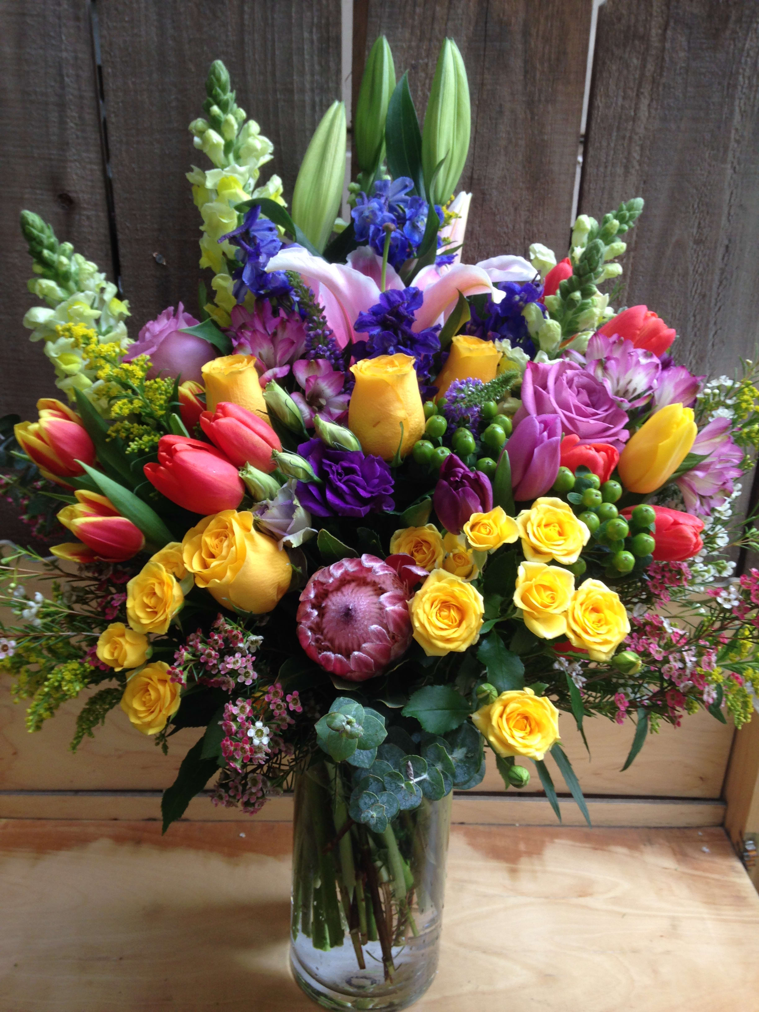 Colorful mixed bouquet in a clear glass vase with roses, tulips, lilies, and snapdragons