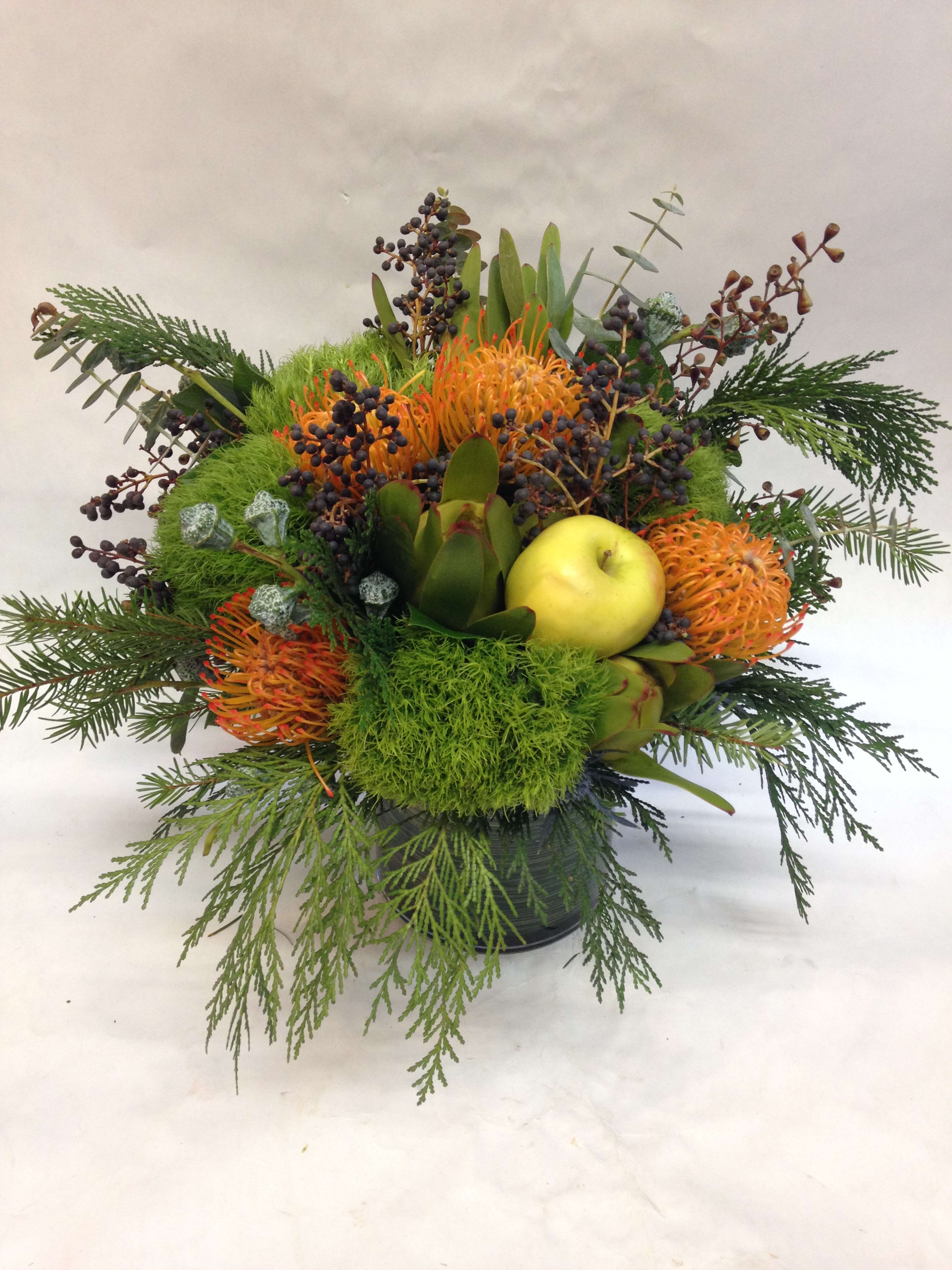 Mixed floral arrangement with orange blooms and a yellow apple in a black container