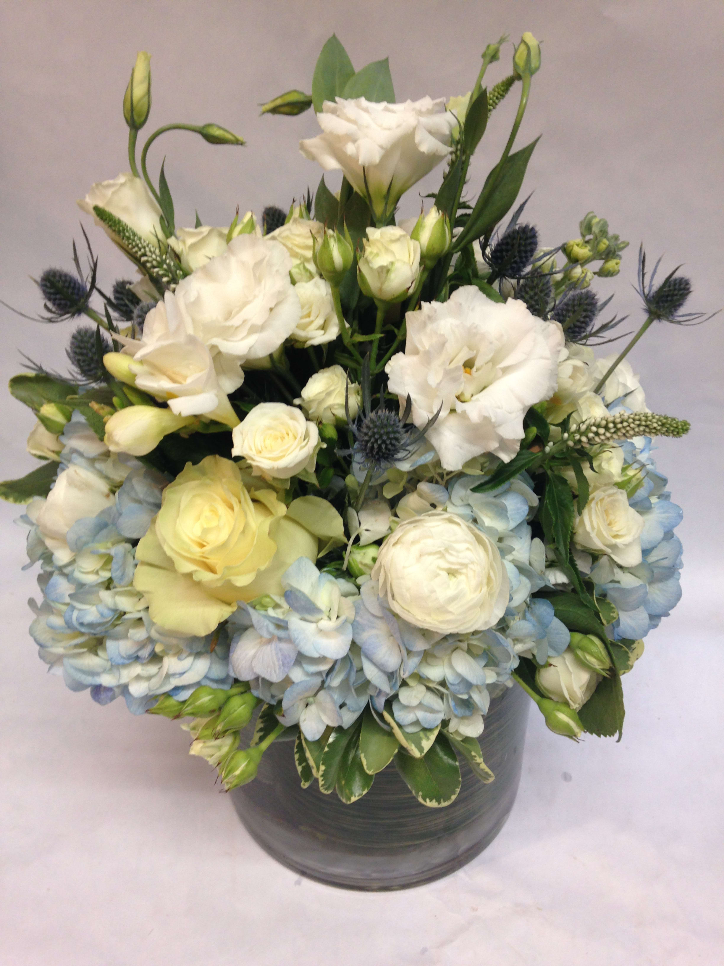 White and pale blue floral arrangement in a gray vase