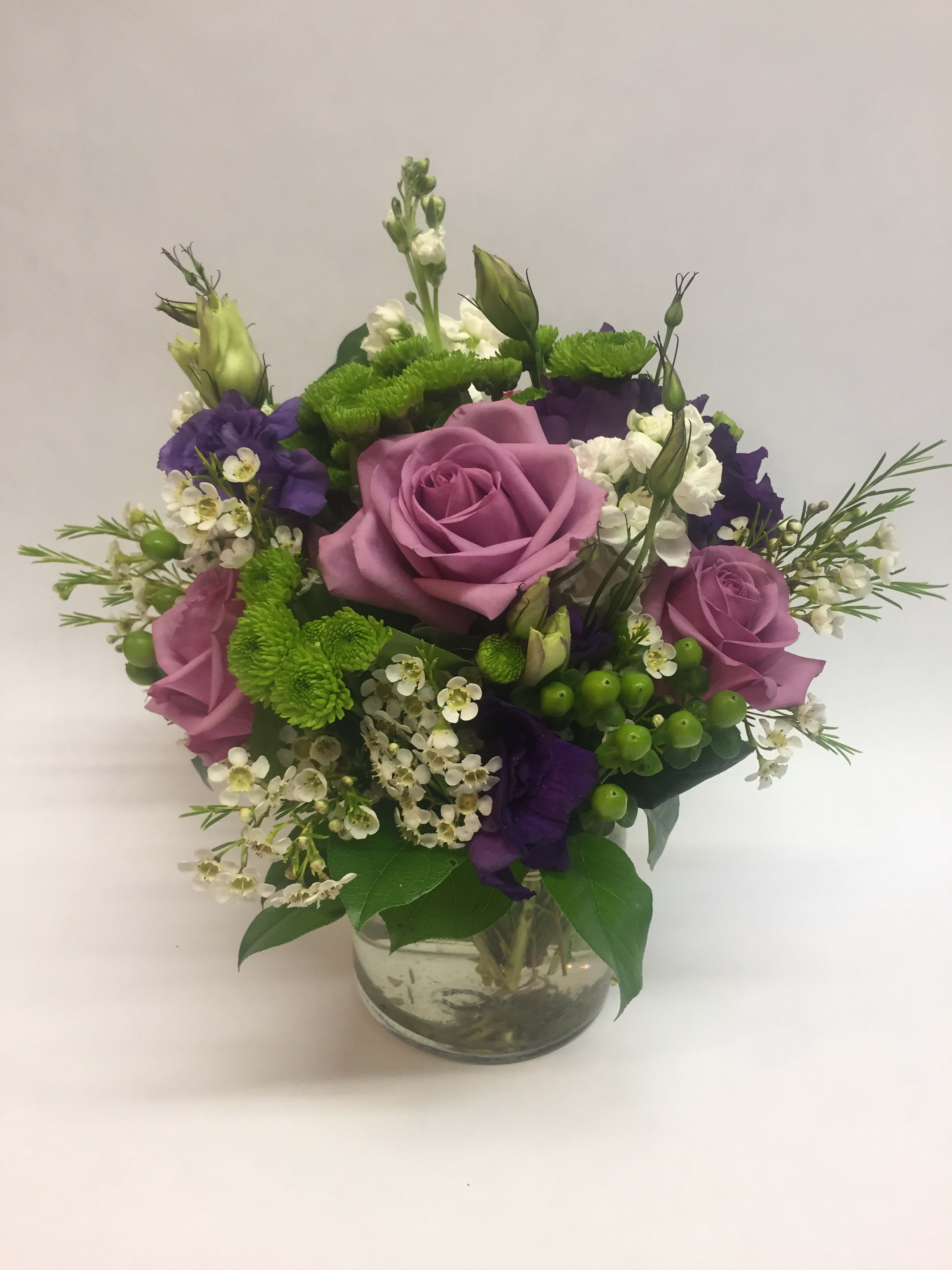 Mixed bouquet of pink roses, purple blooms, and white flowers in a glass vase