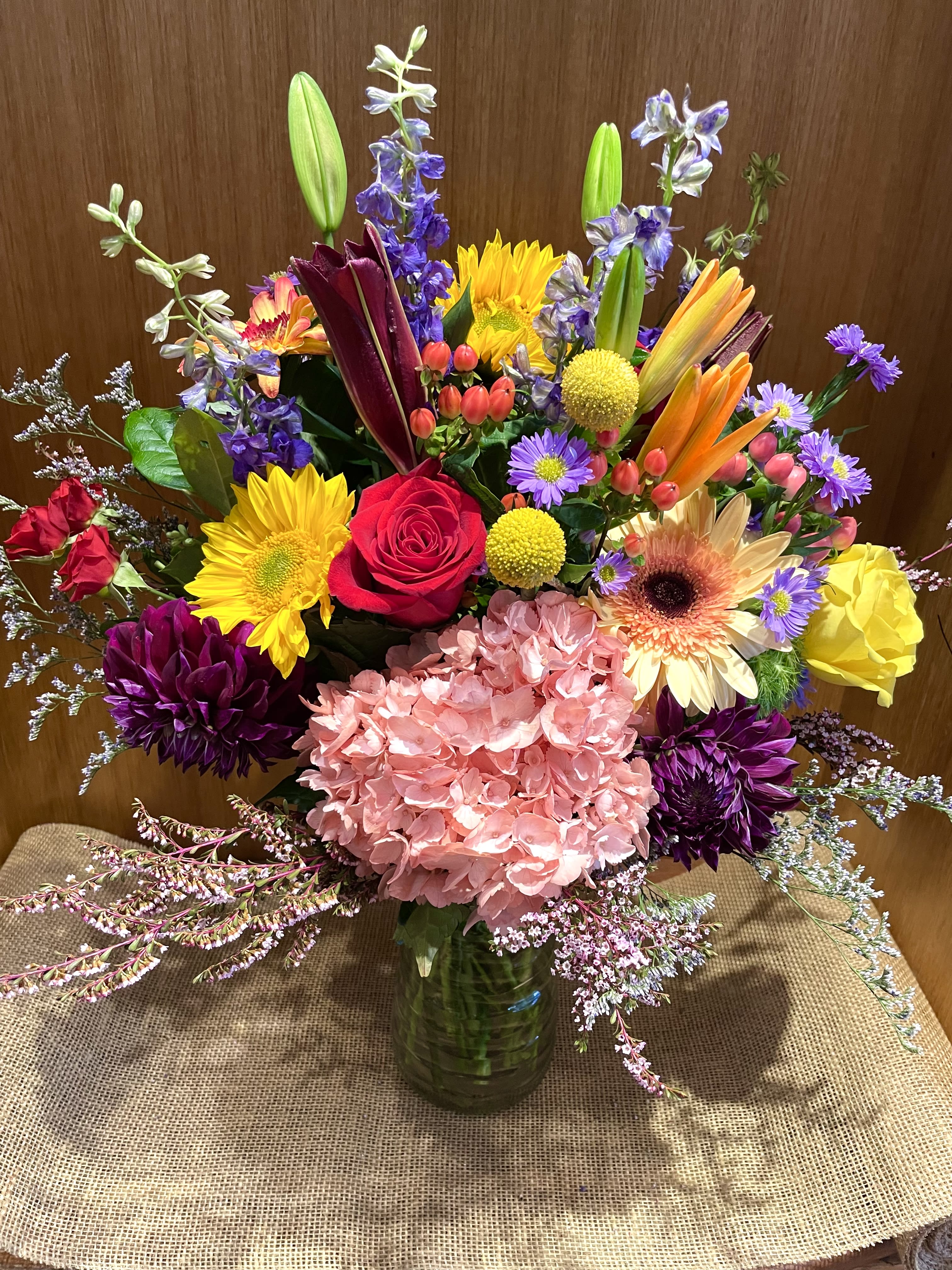 Colorful mixed bouquet in a glass vase with roses, lilies, and hydrangea