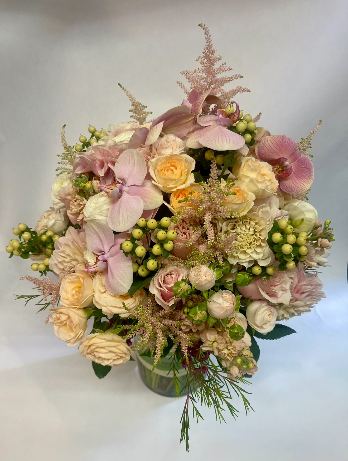 Bouquet of pale pink orchids, cream roses, and green berries in a glass vase