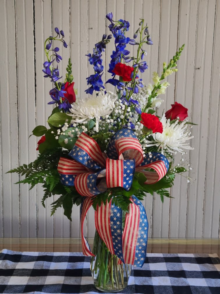 Tall red, white, and blue floral arrangement in a glass vase with patriotic ribbon