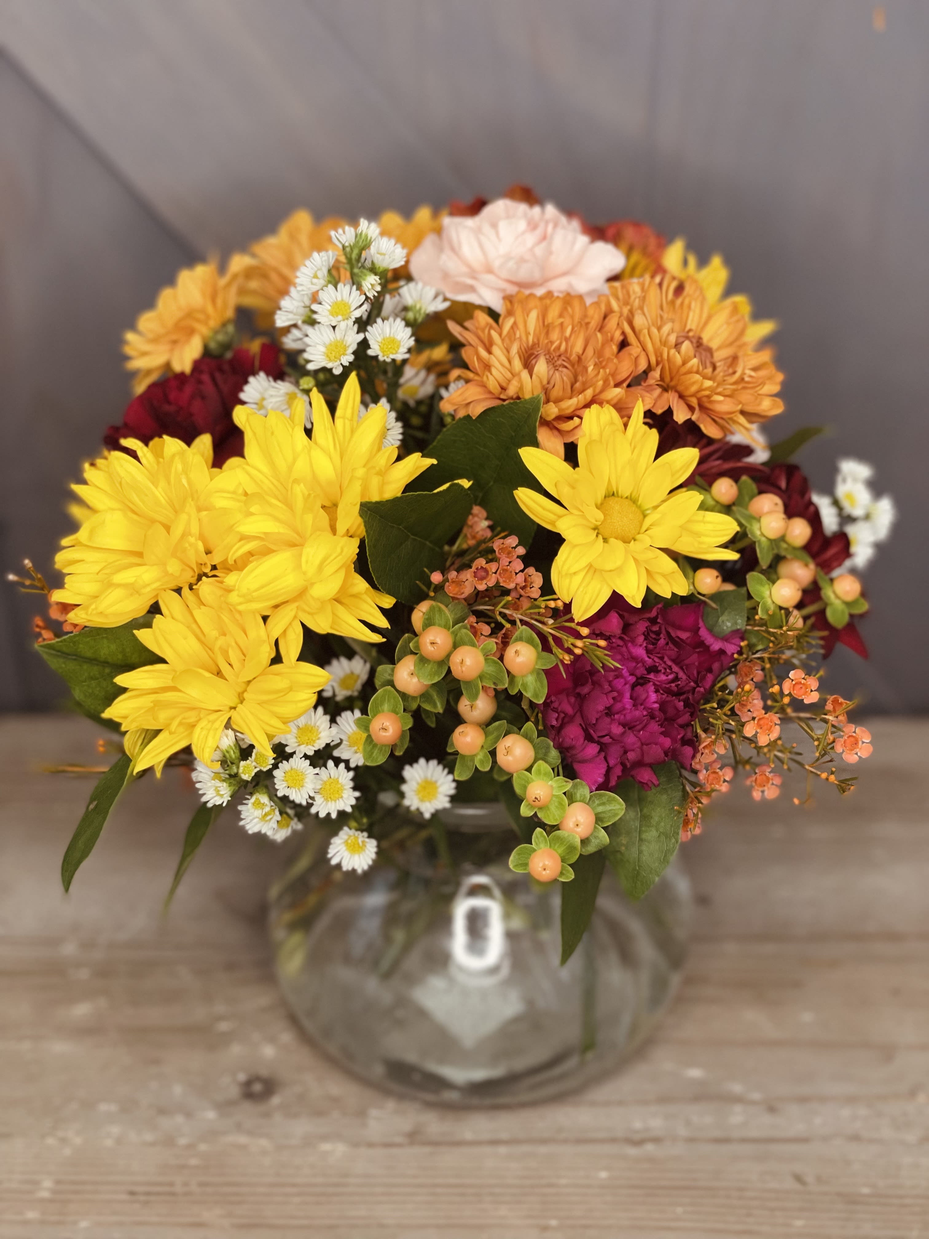 Mixed bouquet of yellow, orange, pink, and white flowers in a clear glass vase