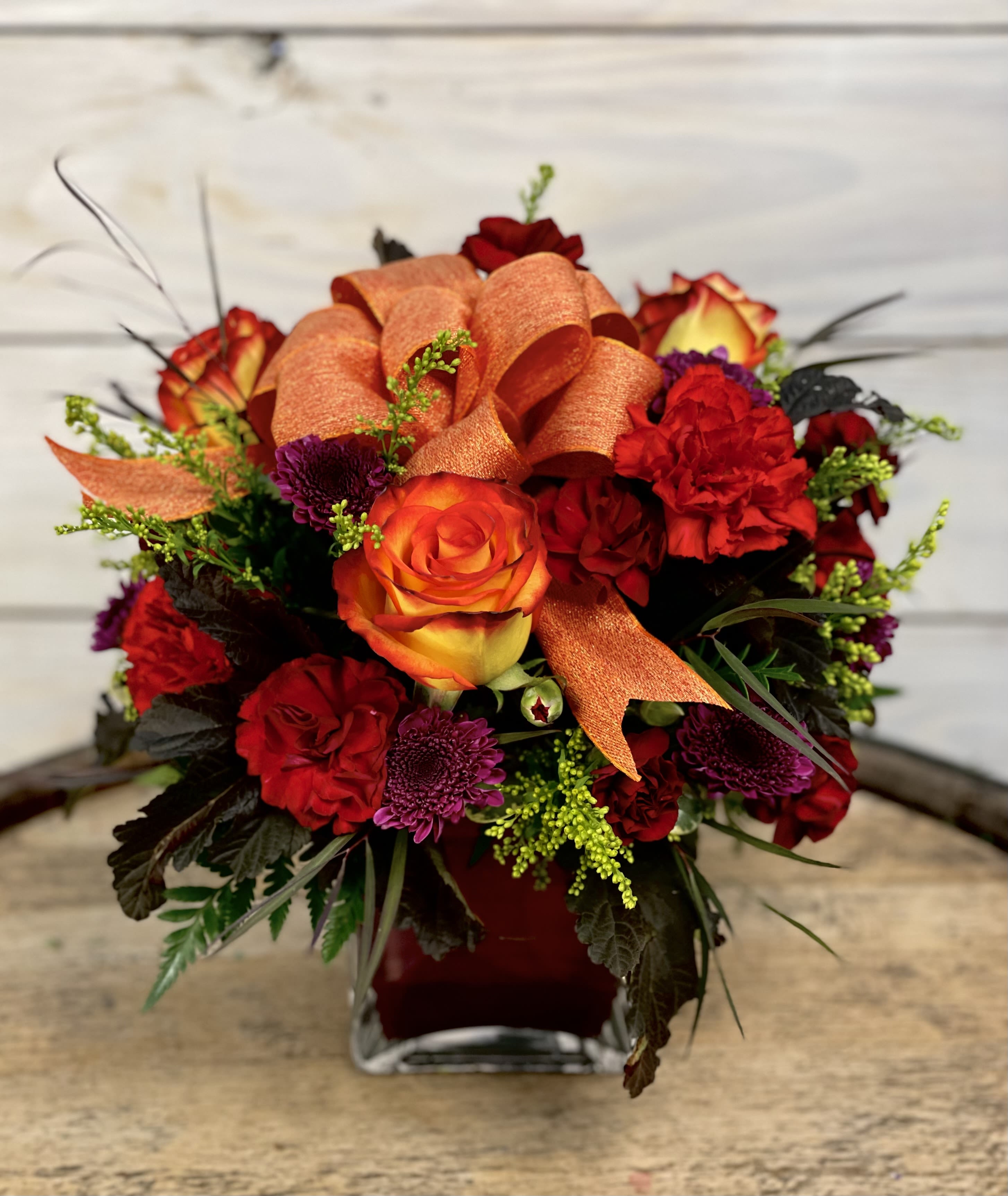 Orange and red rose bouquet in a square glass vase
