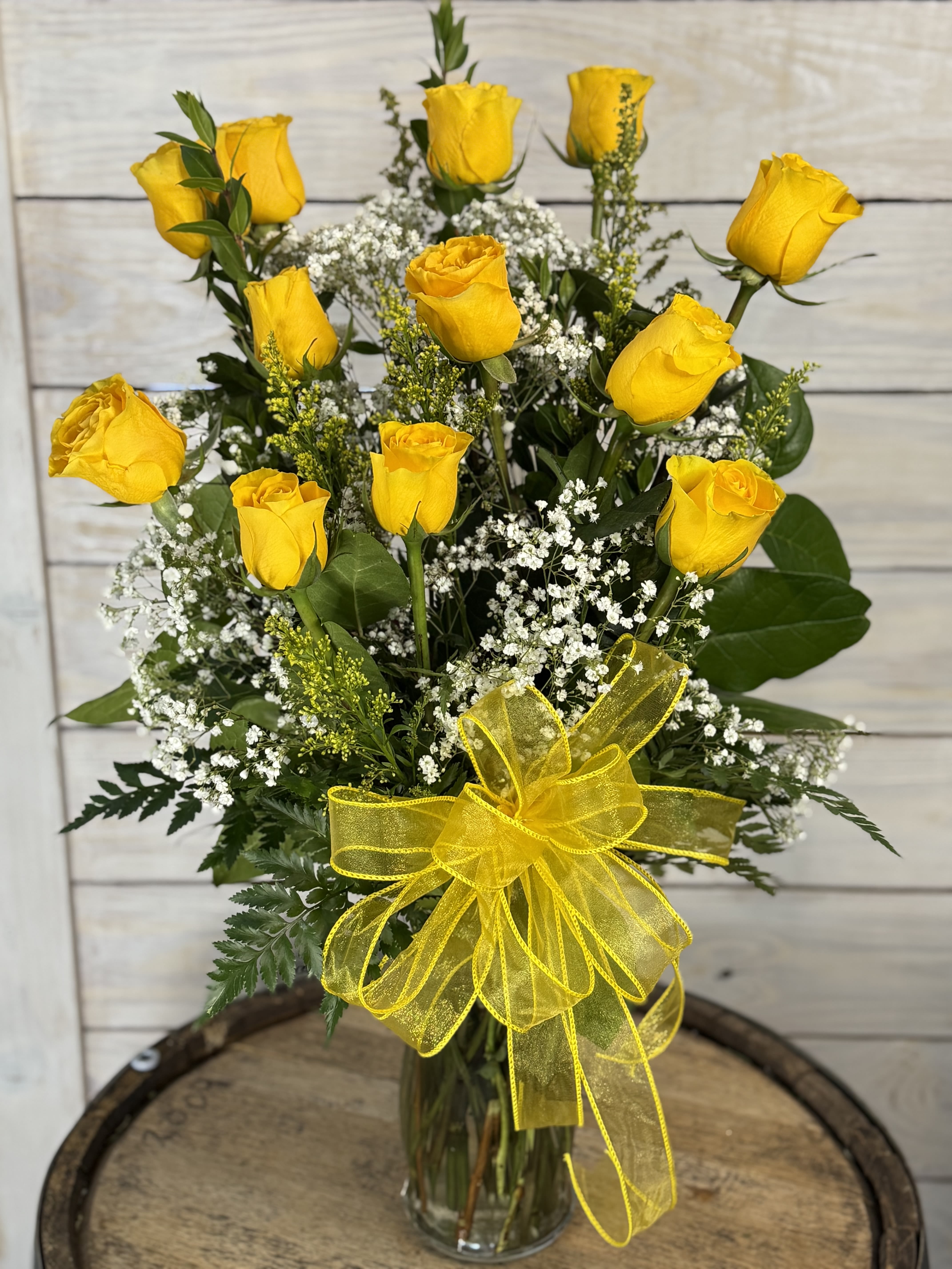 Yellow roses in a glass vase with baby's breath and a yellow ribbon