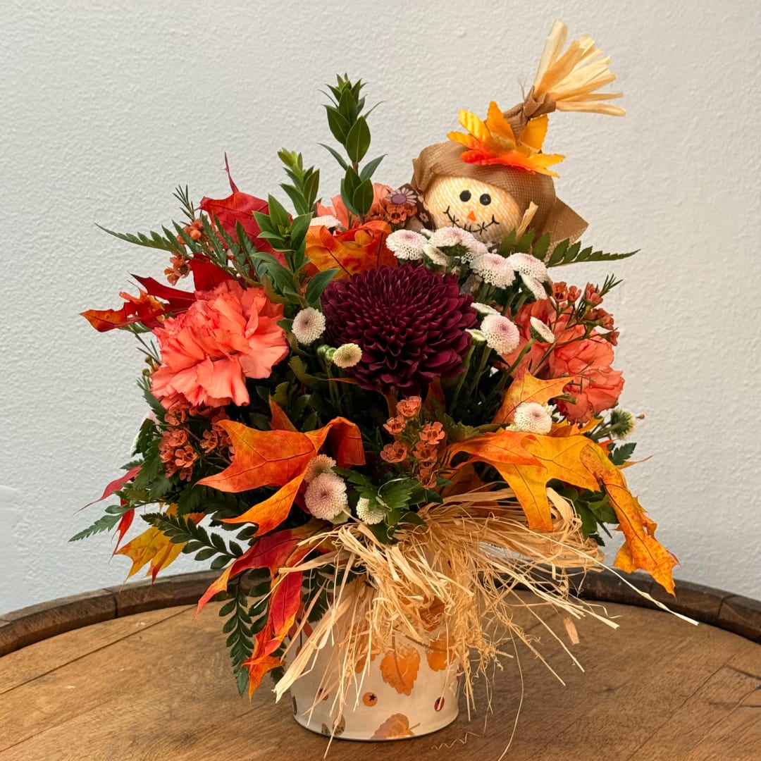Fall floral arrangement with a scarecrow topper in a decorated vase